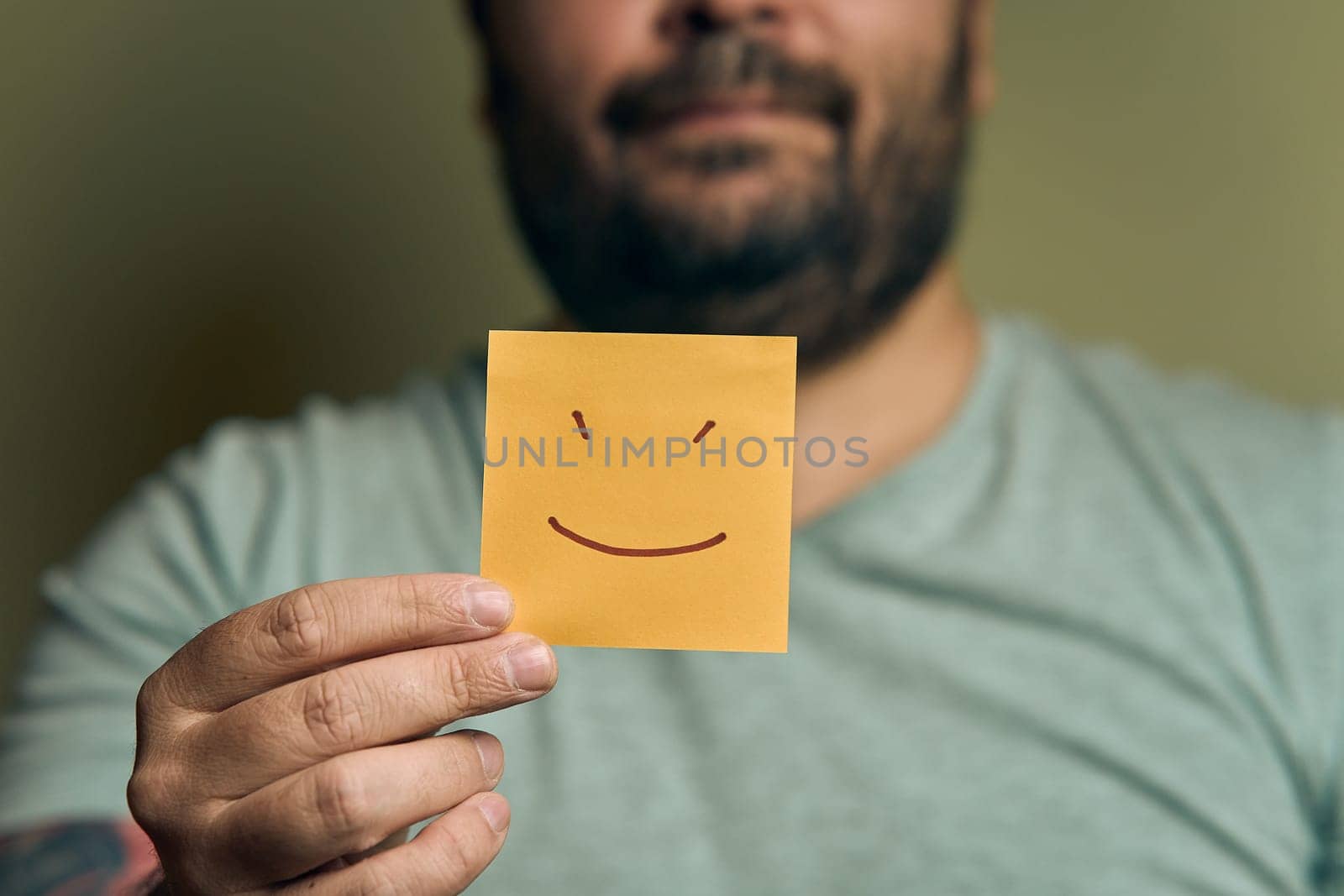 A bearded European man holds a orange sticker in front of him, with a smiley face by snep_photo