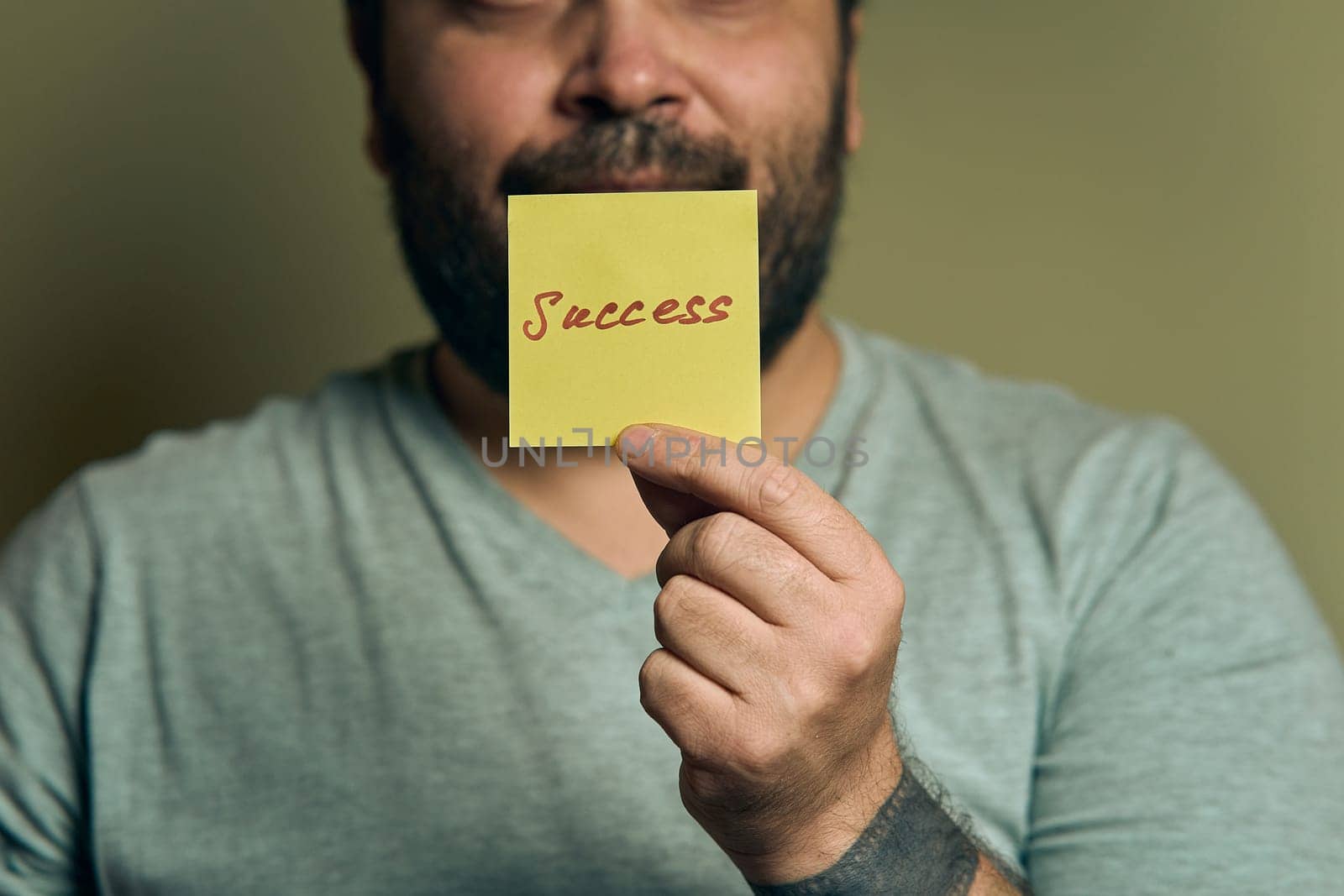 A bearded European man holds a blue sticker in front of him, with the word success