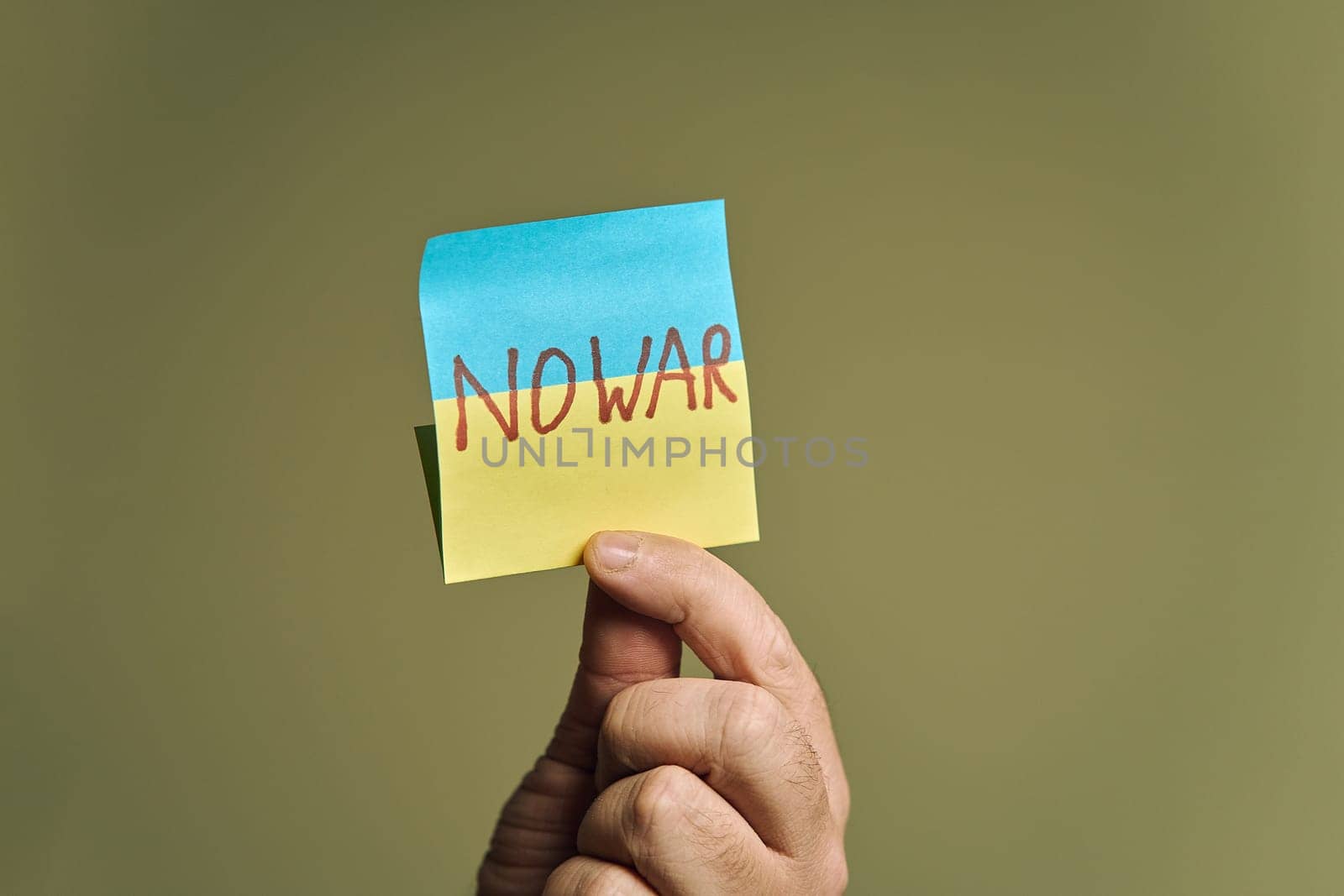 Man's hand holding a sticker, in the form of a Ukrainian flag with the inscription no war by snep_photo