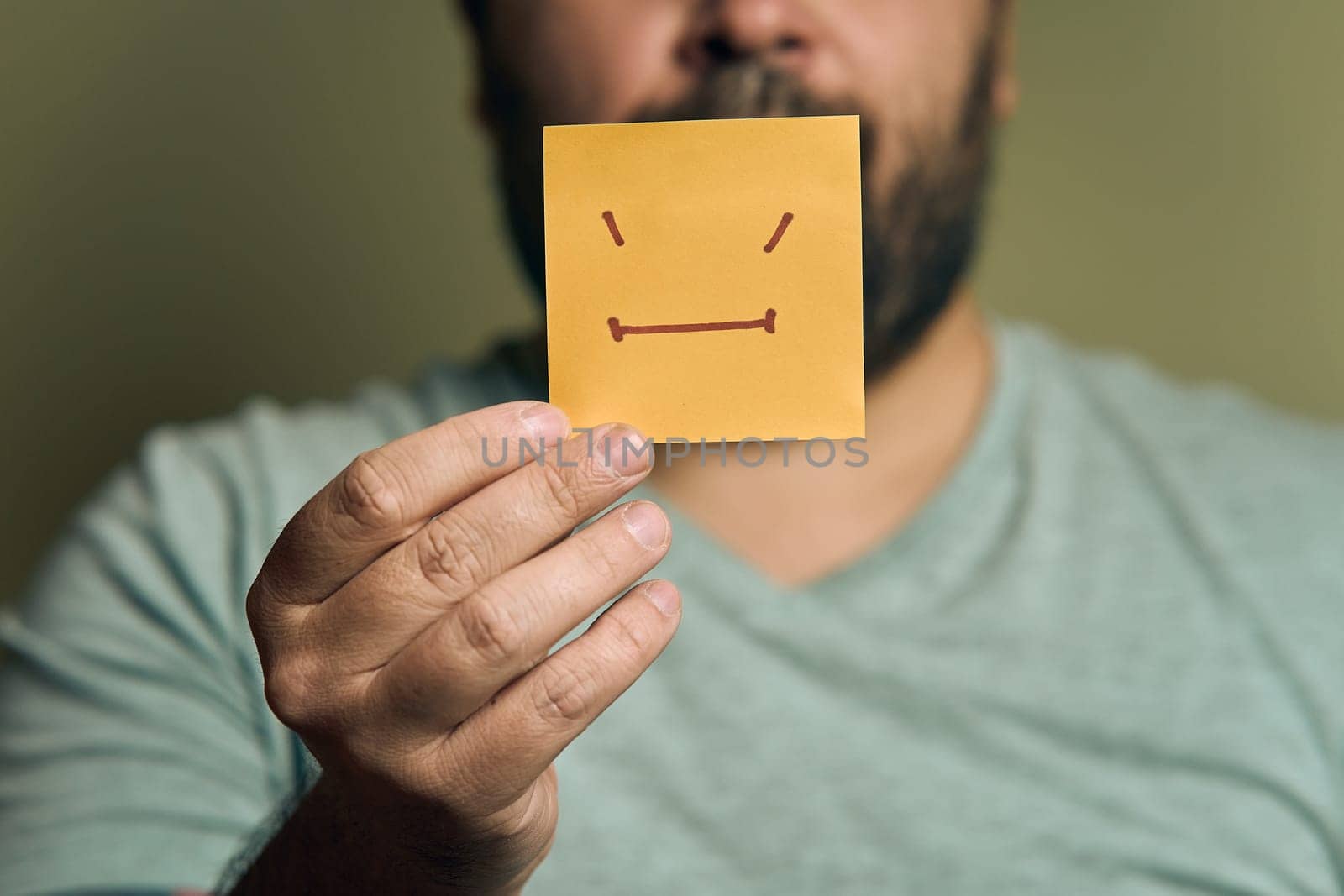 A bearded European man holds a orange sticker in front of him, with an unhappy smiley