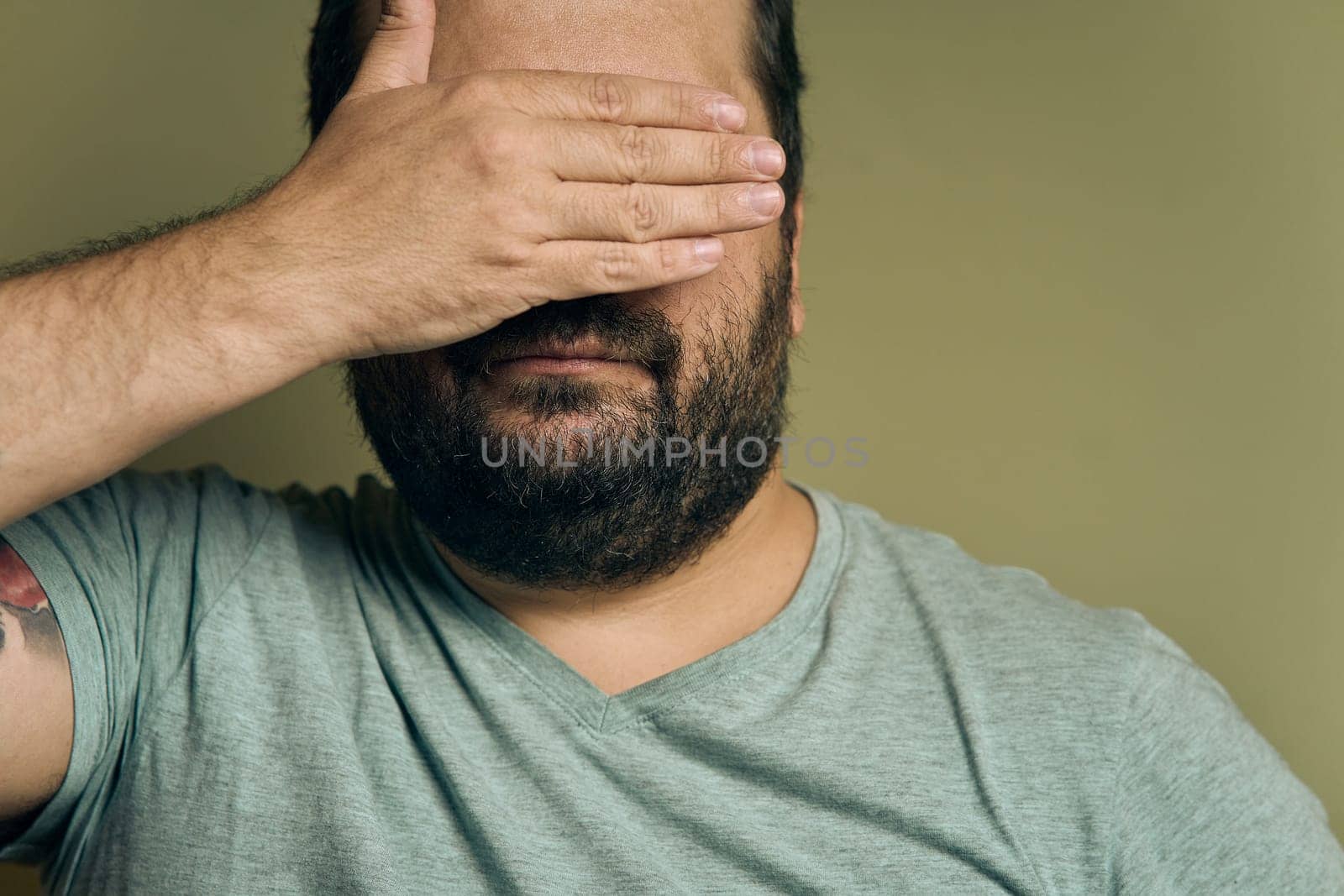 A bearded European man covers his eyes with his hand by snep_photo