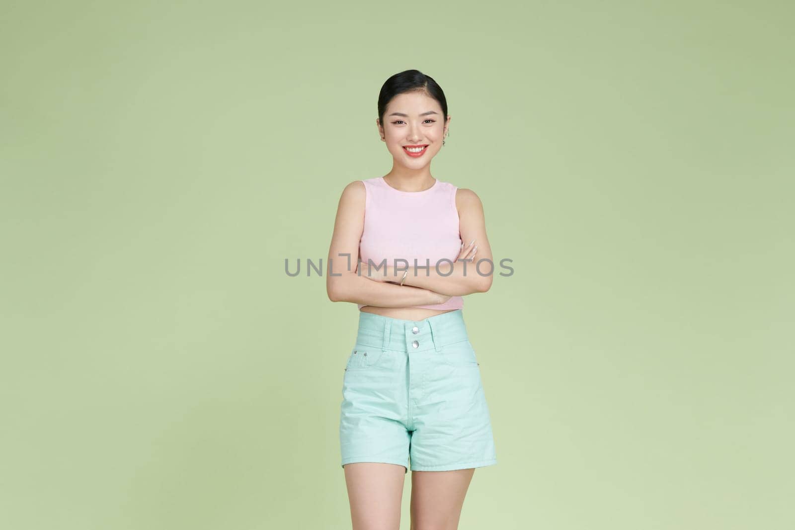Smiling woman with arms crossed standing against pastel green background