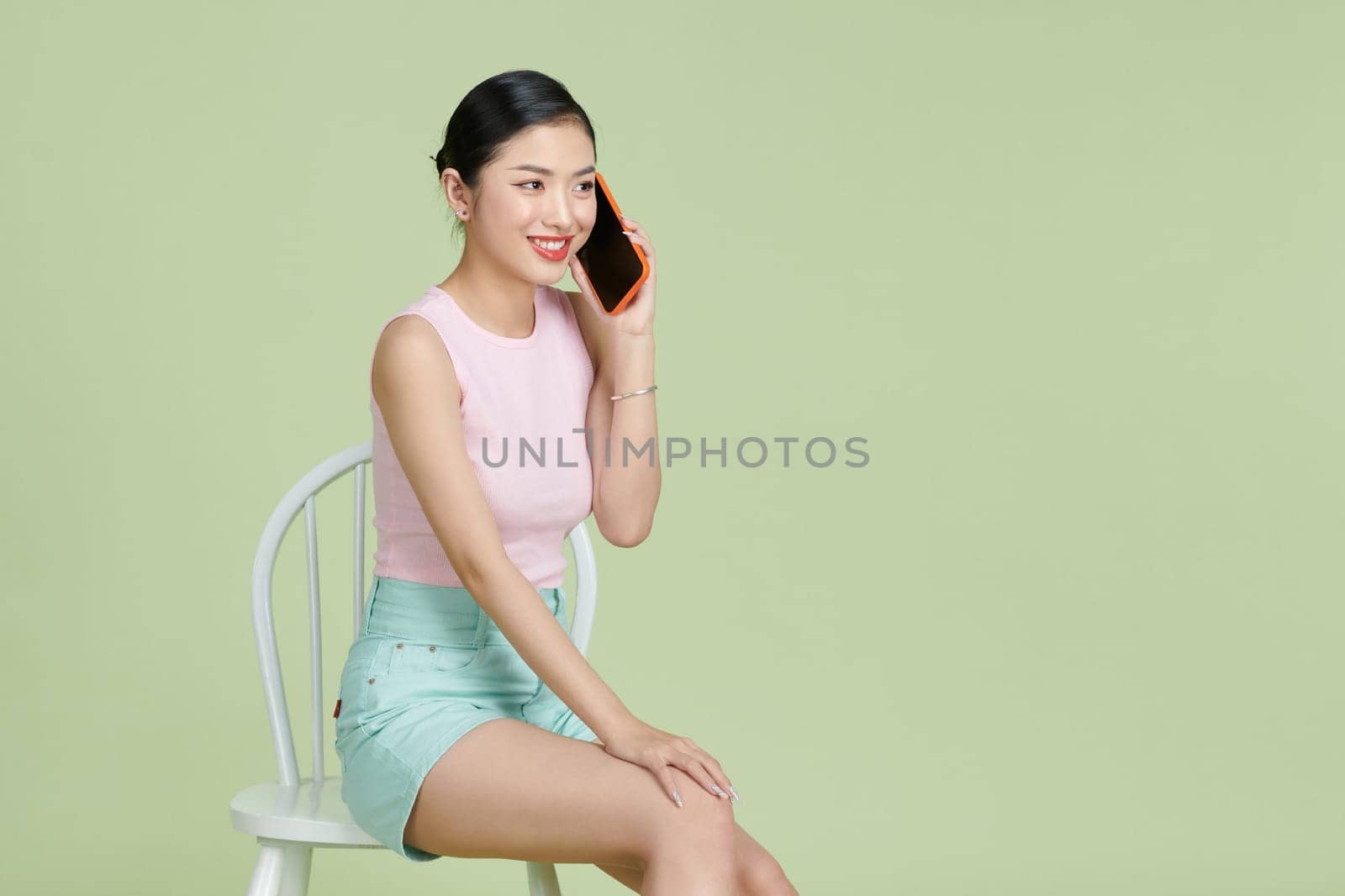 Pretty smiling girl talking on the smartphone and sitting on the chair