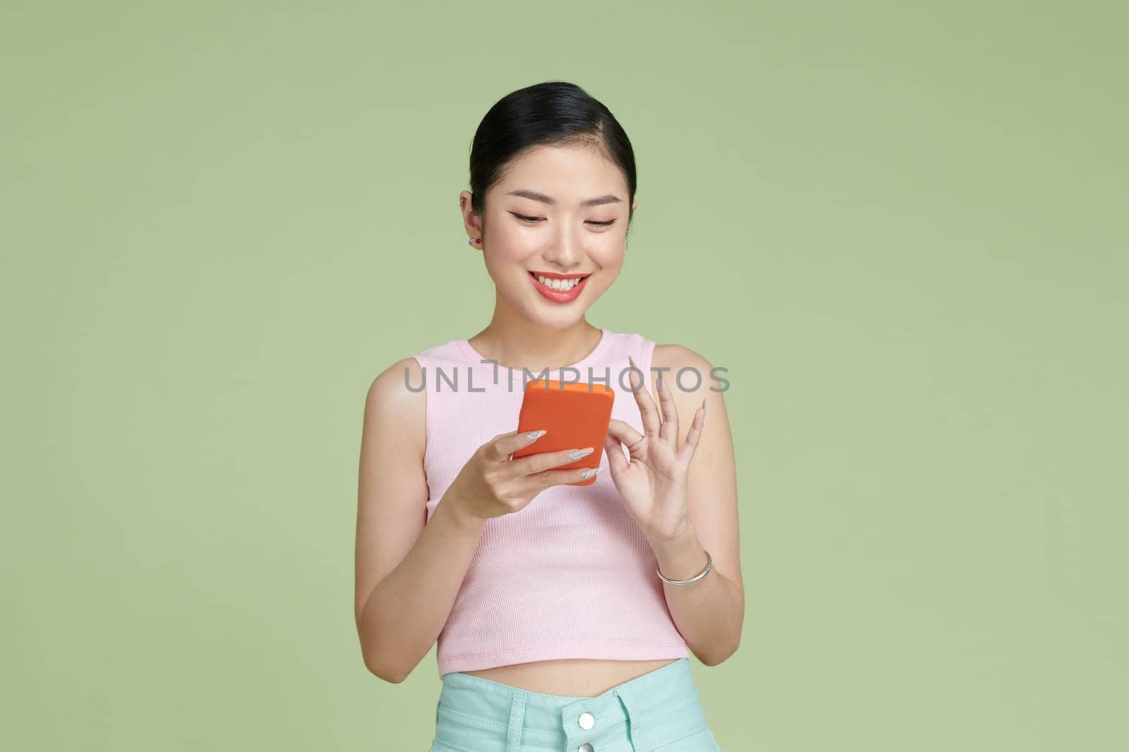 Happy Asian portrait beautiful cute young woman smiling excited typing text message on smart mobile phone 