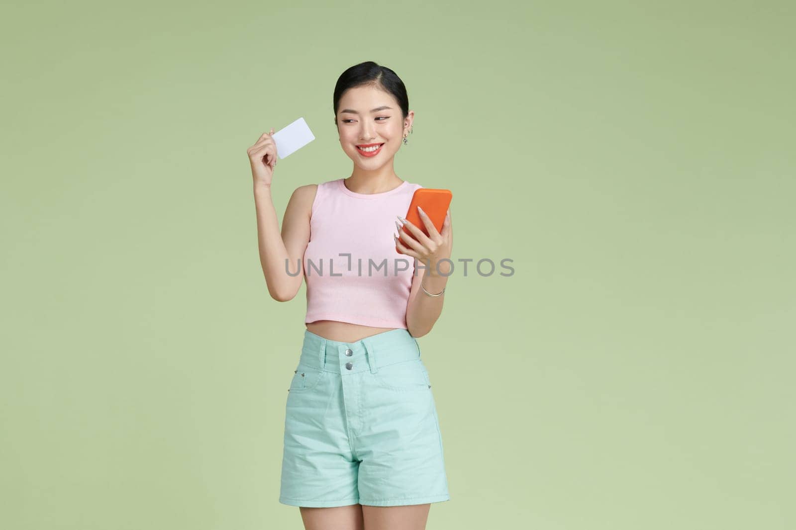 Portrait of a happy young girl showing plastic credit card while holding mobile phone