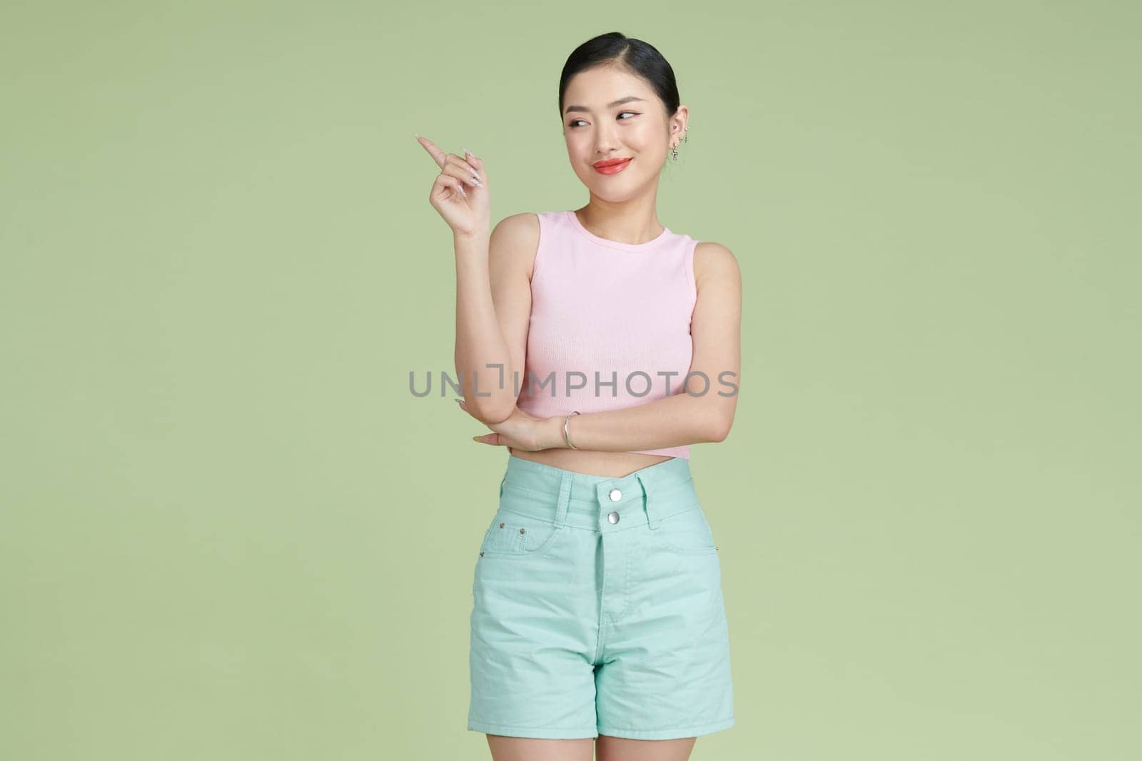 Young elegant woman pointing at plastic green background