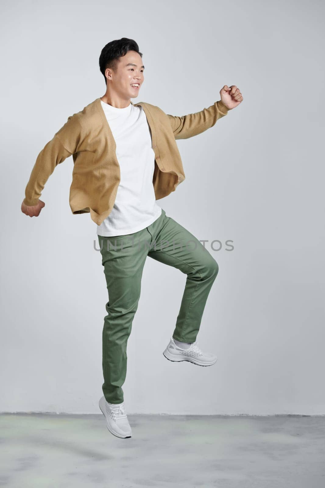 Happy energetic young Asian man jumping yelling and clenching fists isolated