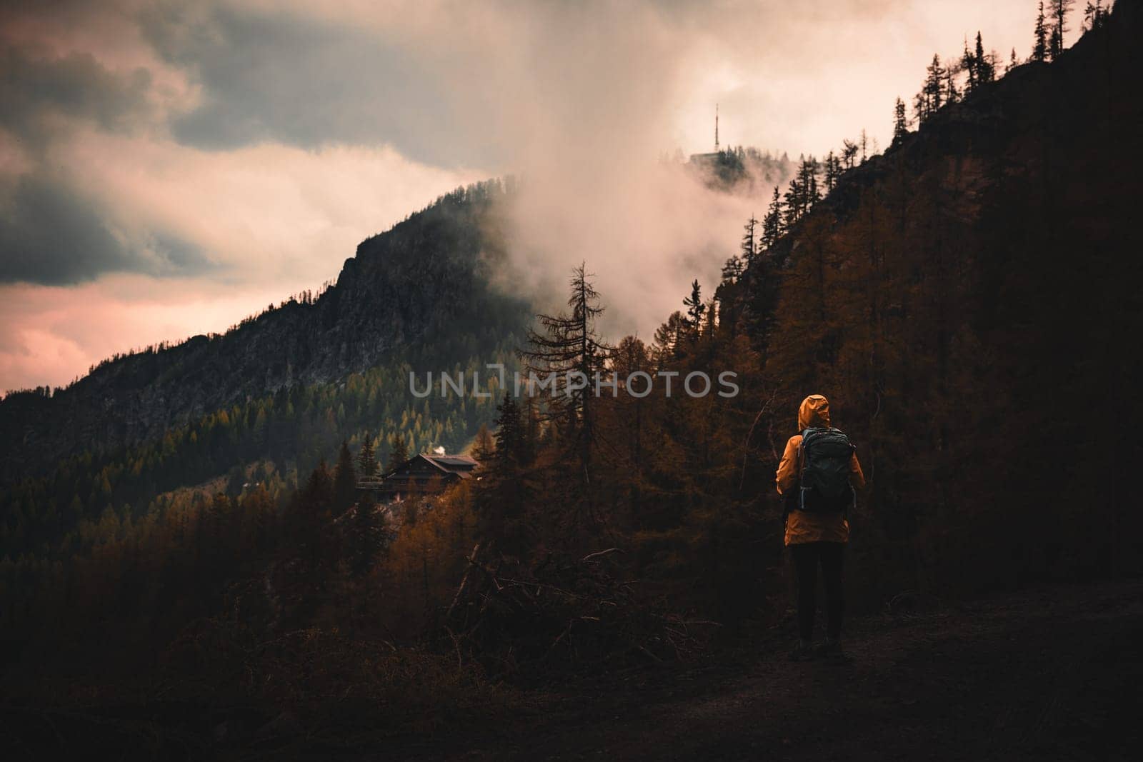 A traveler woman in a yellow jacket is looking at an autumn view while exploring Alpine mountains. by Kustov