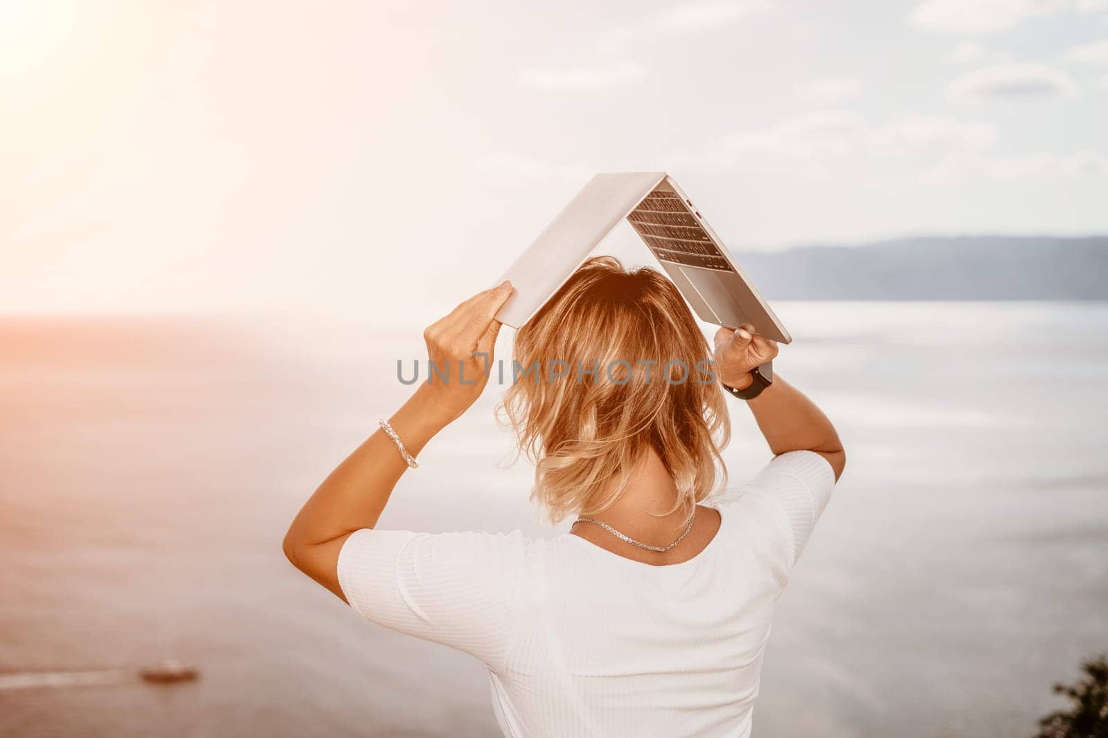 Digital nomad, Business woman working on laptop by the sea. Pretty lady typing on computer by the sea at sunset, makes a business transaction online from a distance. Freelance remote work on vacation