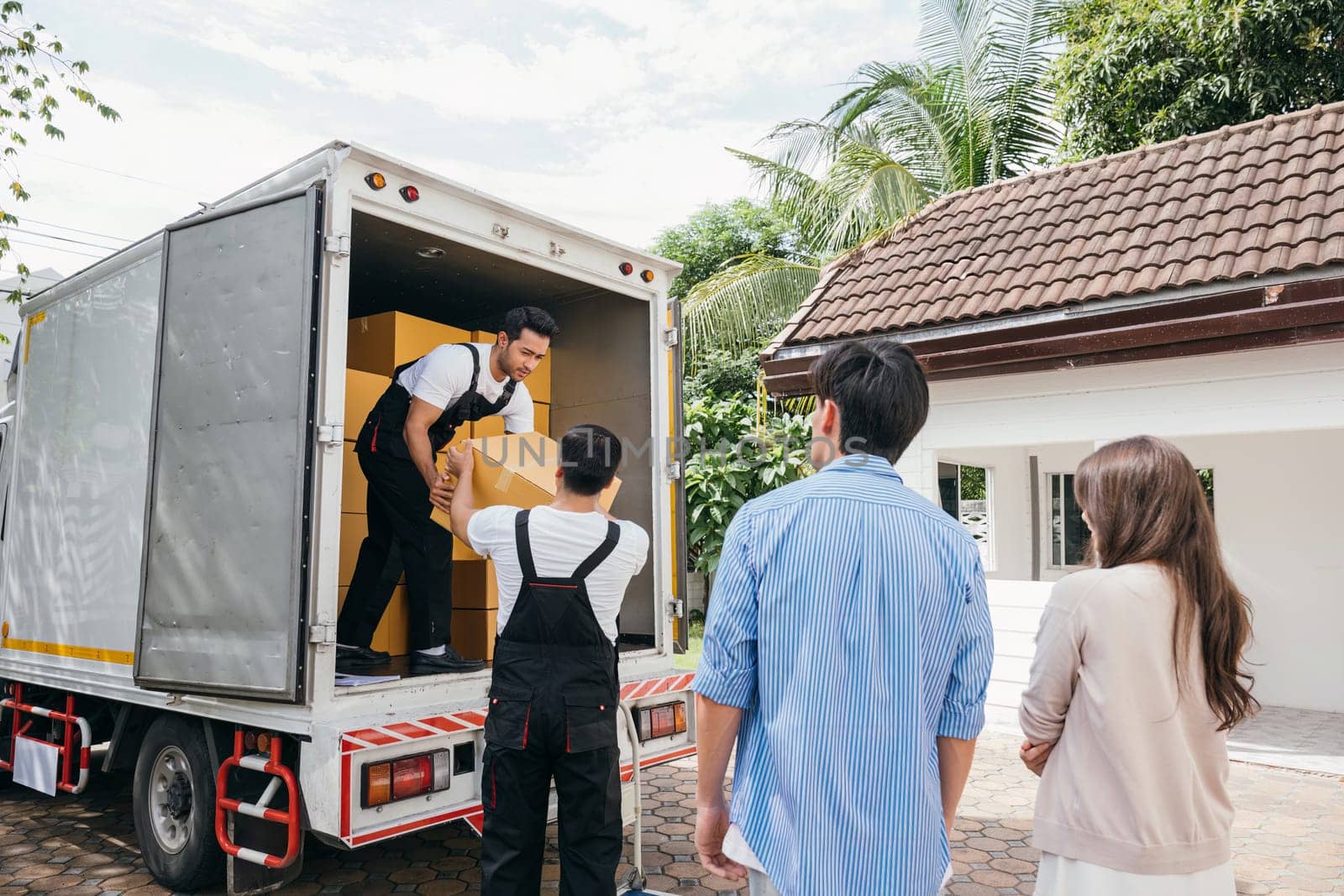Team of workers assists a couple in moving into their new home. Together they unload and lift cardboard boxes showcasing professional and efficient delivery service. Moving Day Concept by Sorapop