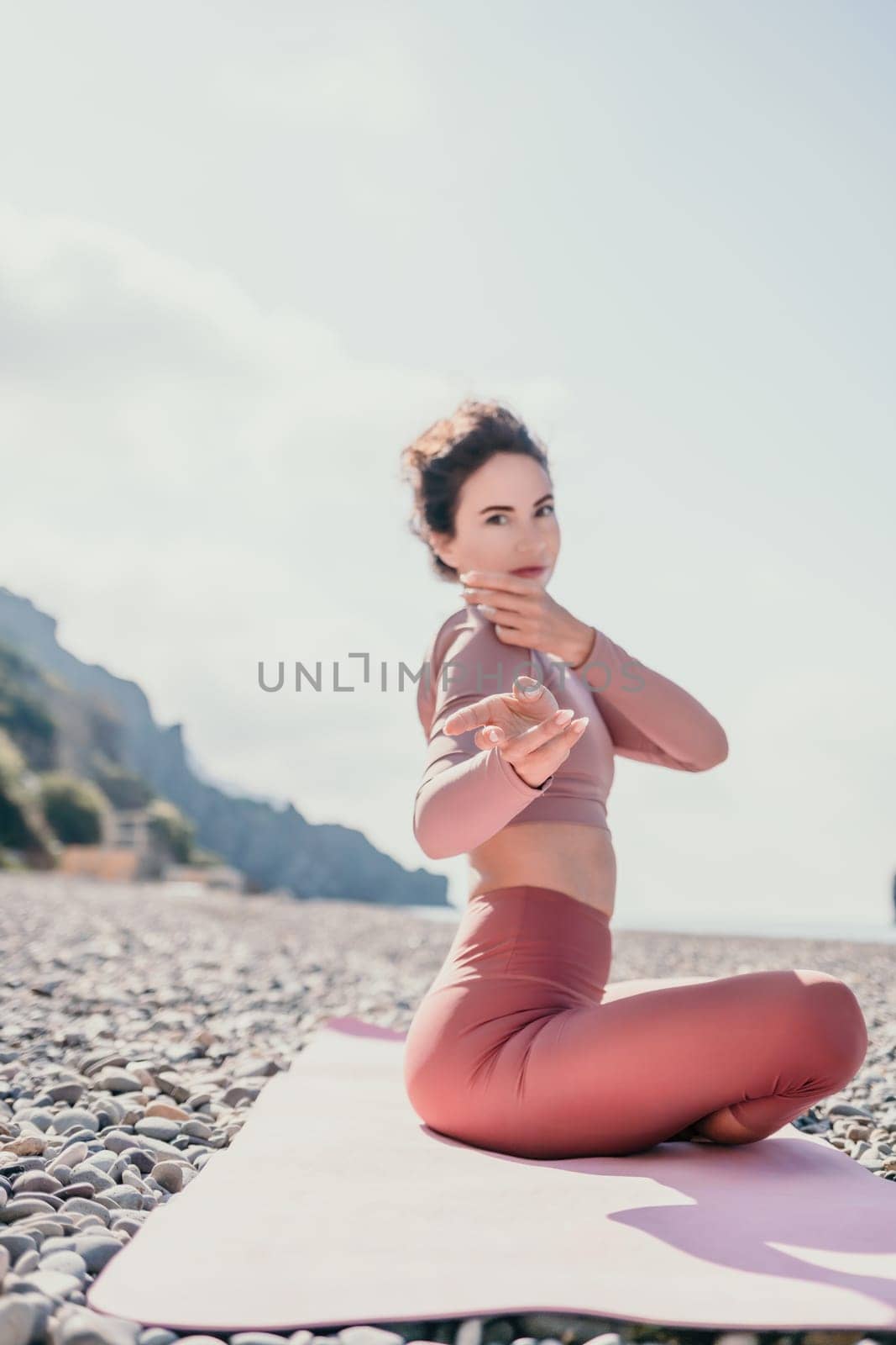 Middle aged well looking woman with black hair, fitness instructor in leggings and tops doing stretching and pilates on yoga mat near the sea. Female fitness yoga routine concept. Healthy lifestyle by panophotograph