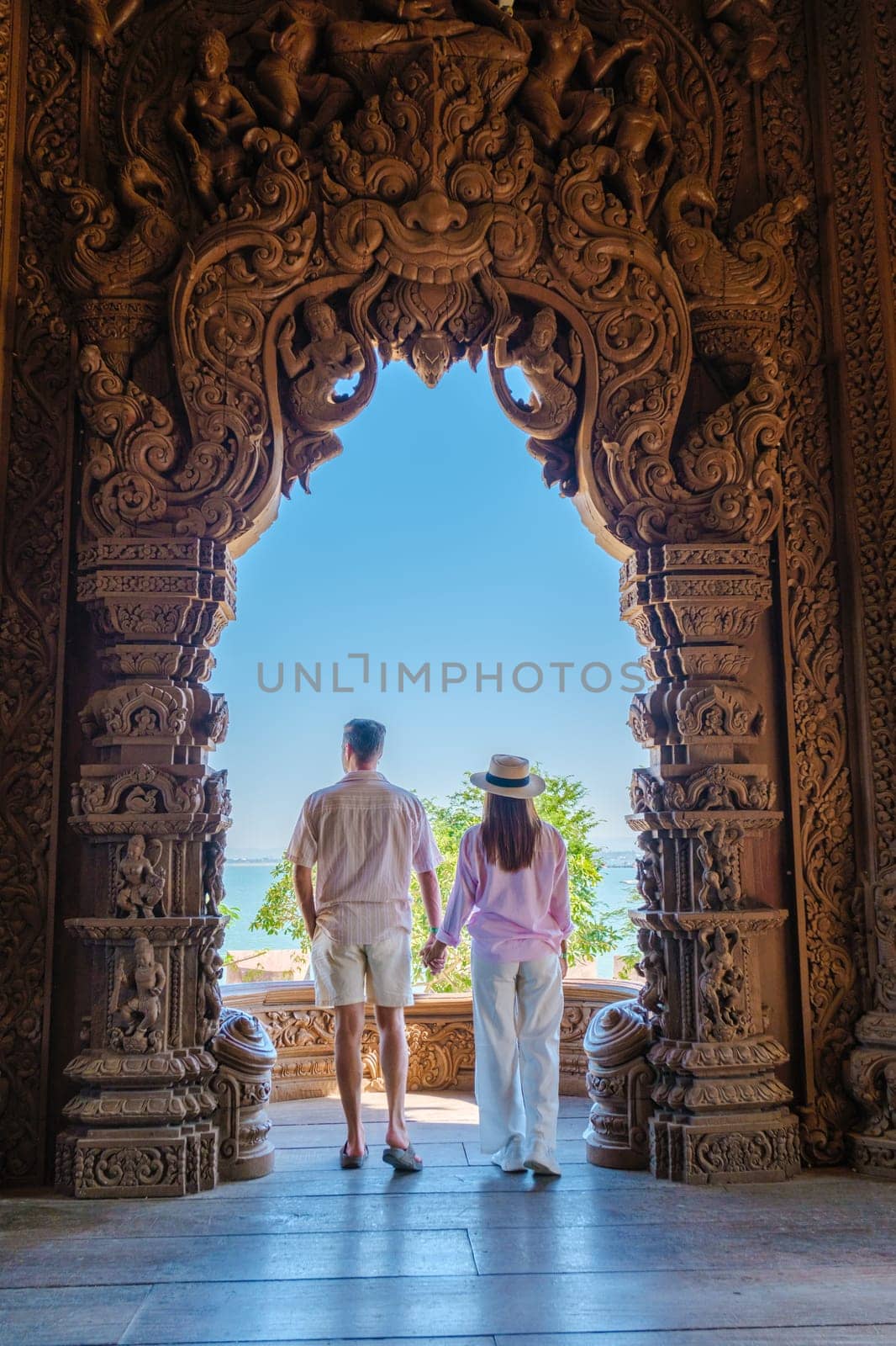 A diverse multiethnic couple of men and women visit The Sanctuary of Truth wooden temple in Pattaya Thailand, wooden temple of Pattaya