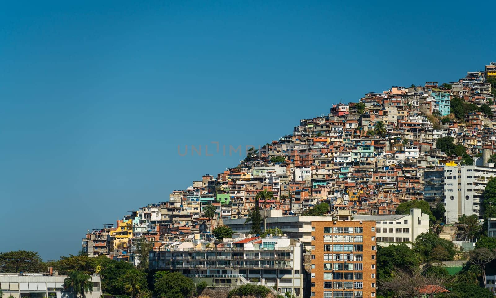 A vivid favela on a hill contrasts with nearby modern homes on a sunny day.