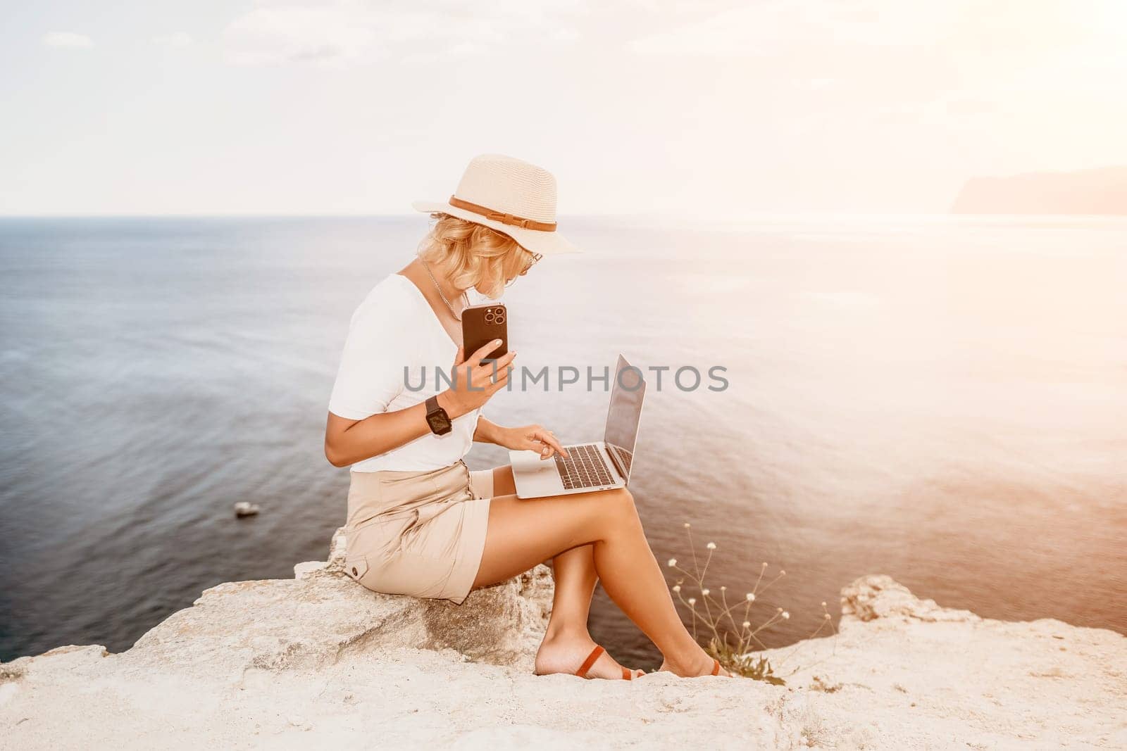 Digital nomad, Business woman working on laptop by the sea. Pretty lady typing on computer by the sea at sunset, makes a business transaction online from a distance. Freelance, remote work on vacation by panophotograph