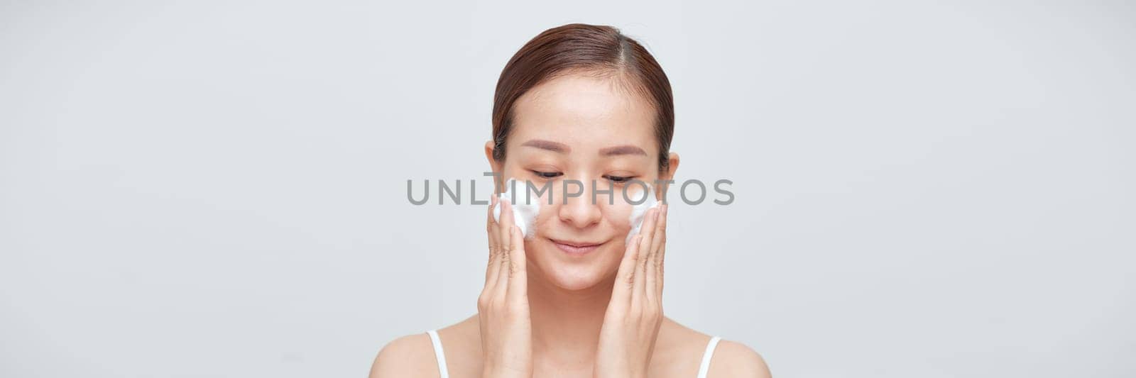 Satisfied girl with bare shoulders applying cleansing beauty product on cheeks. Banner by makidotvn