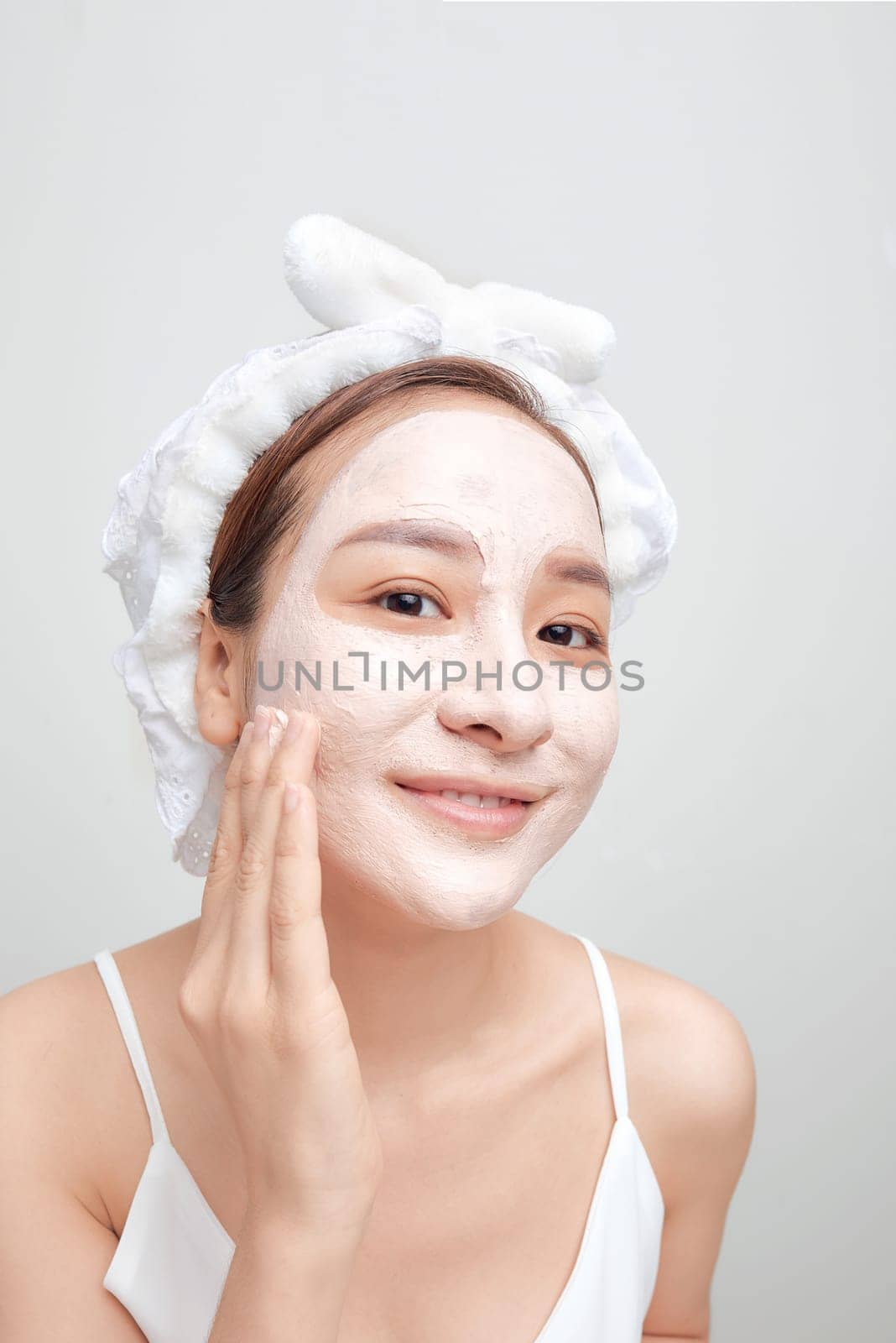A woman with a clay cosmetic mask in a white towel on her head on a white background. Banner by makidotvn