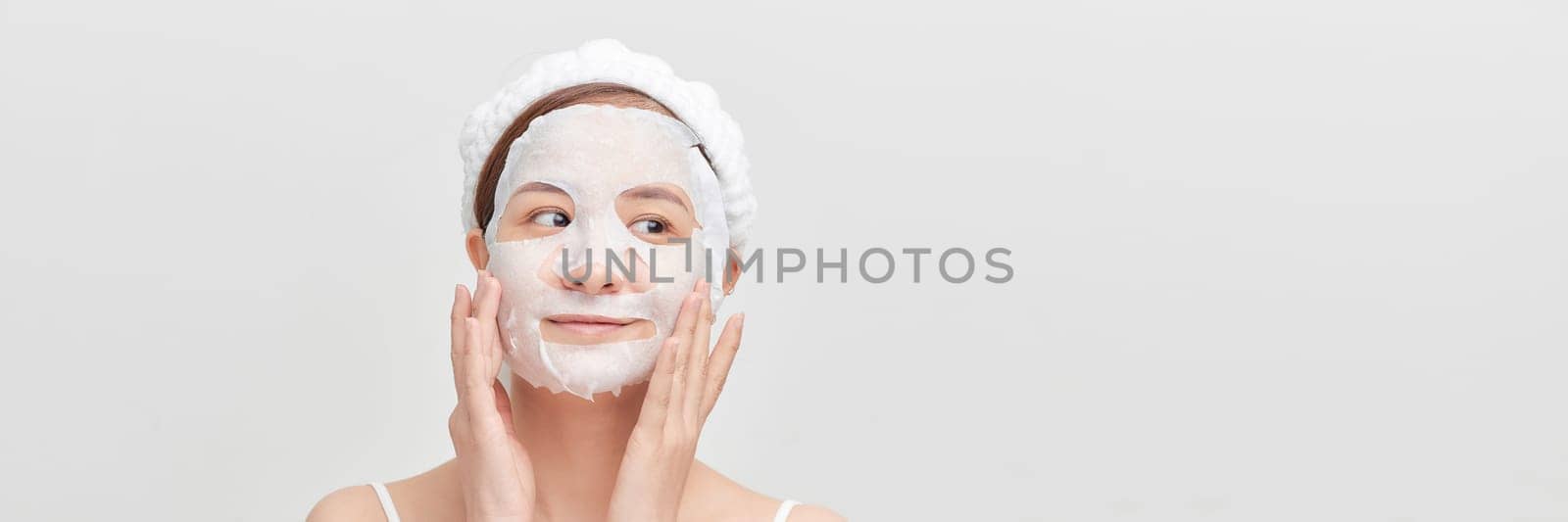 Woman with a cloth moisturizing mask on her face isolated on white banner background by makidotvn