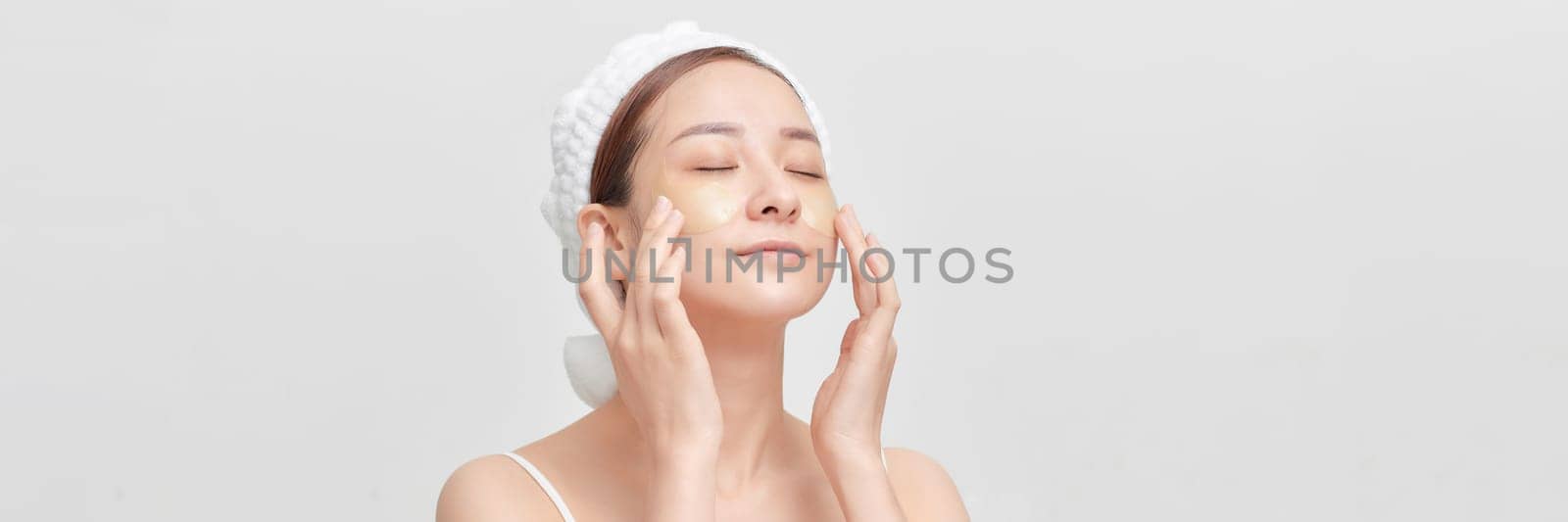 Satisfied woman with collagen patches on clear radiant face skin on light background.