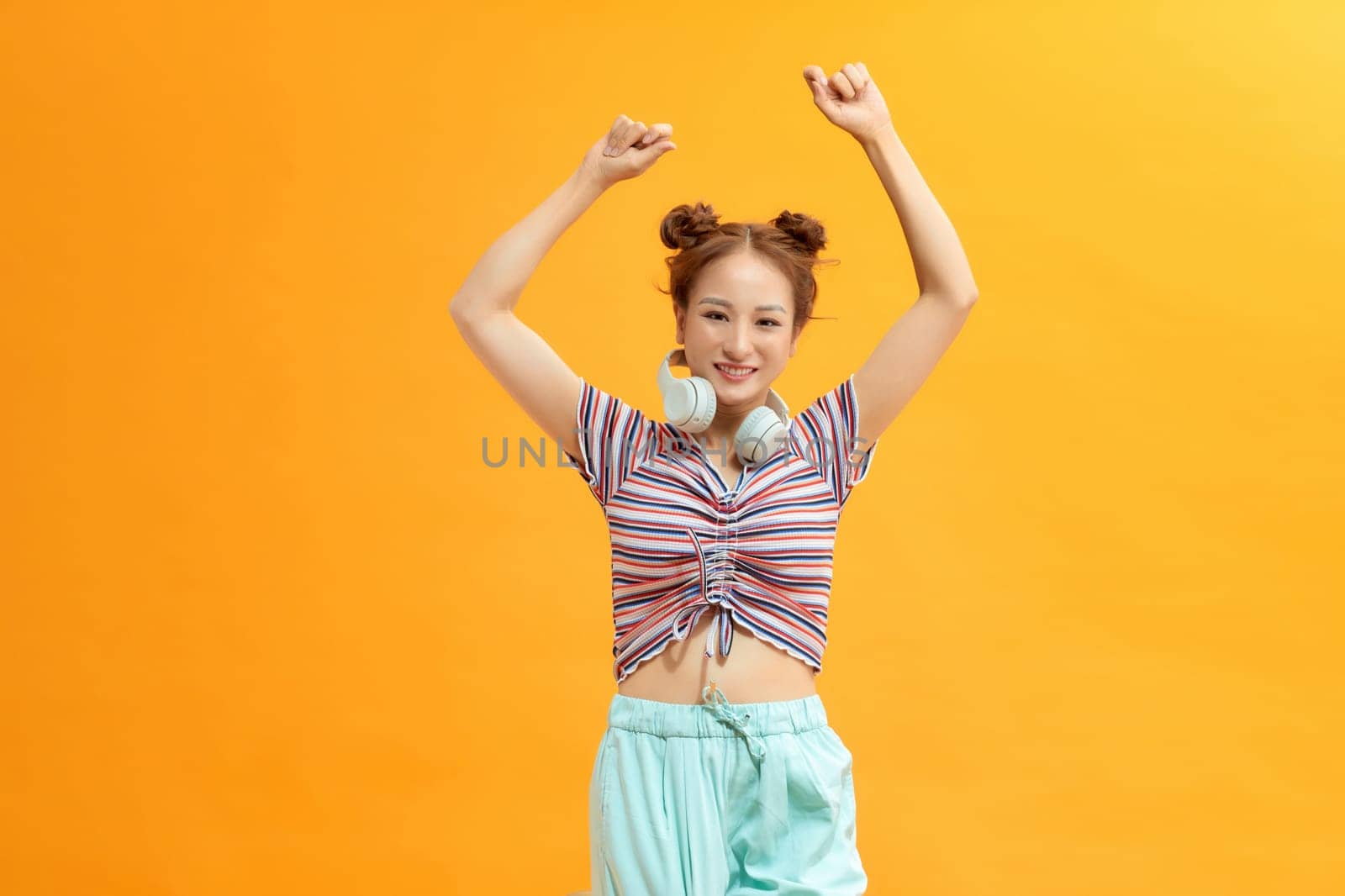 Girl dancing on yellow background wearing headphones on neck, lifestyle concept, copy space by makidotvn