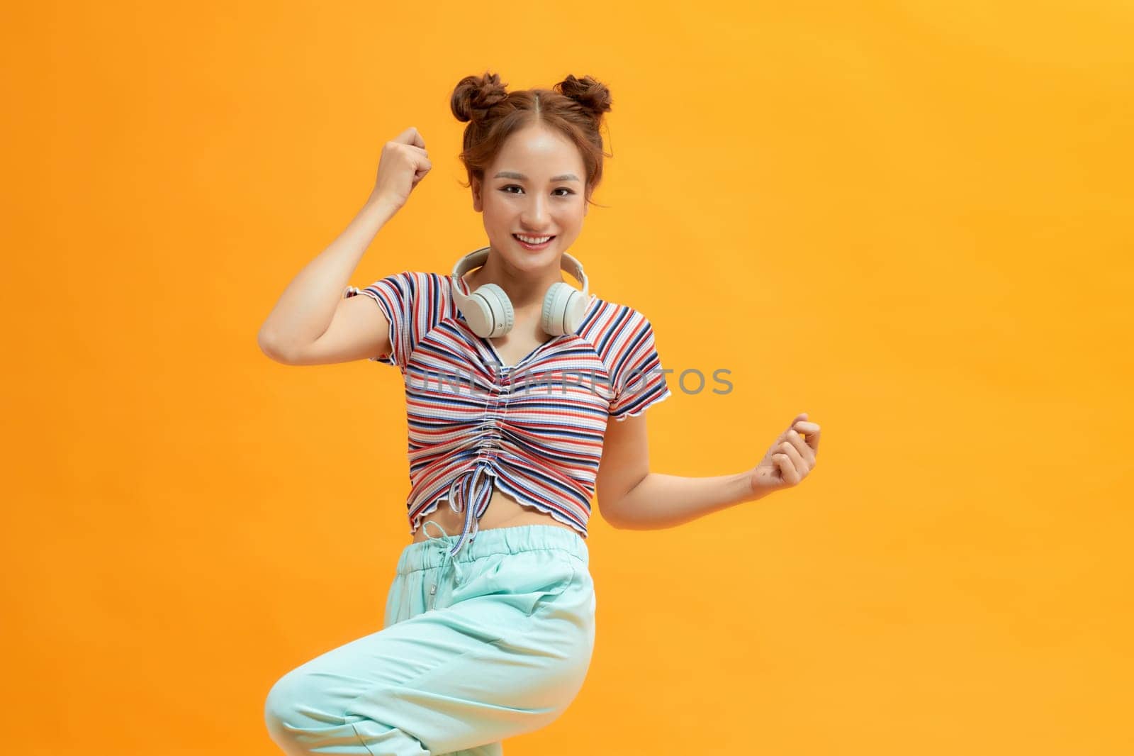 Young women with headphone on her neck and dancing with happiness isolated on yellow background. by makidotvn