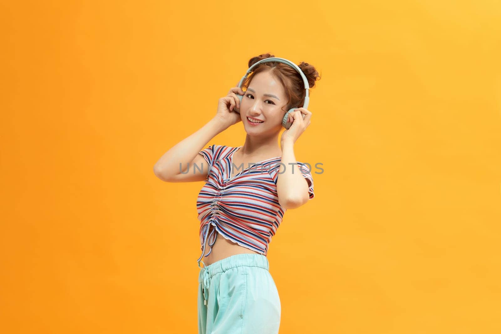 Young satisfied fun woman wear headphones listen to music isolated on yellow background