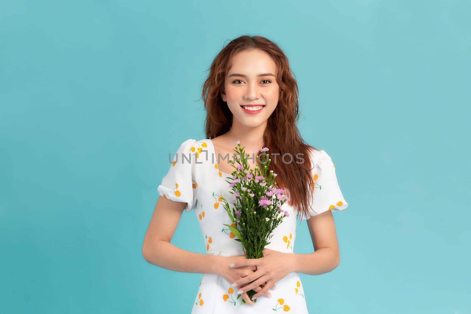 A beautiful young asian woman posing isolated over blue background holding flowers.