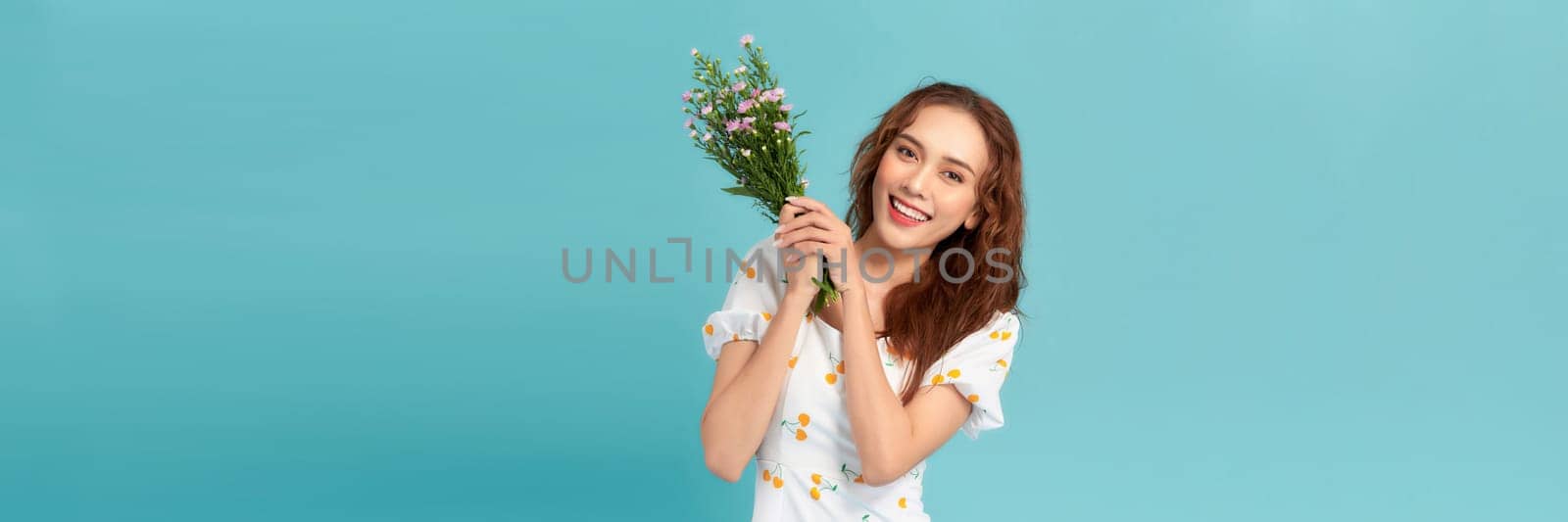 Beautiful cheerful young girl wearing summer dress, holding bouquet of wildflowers