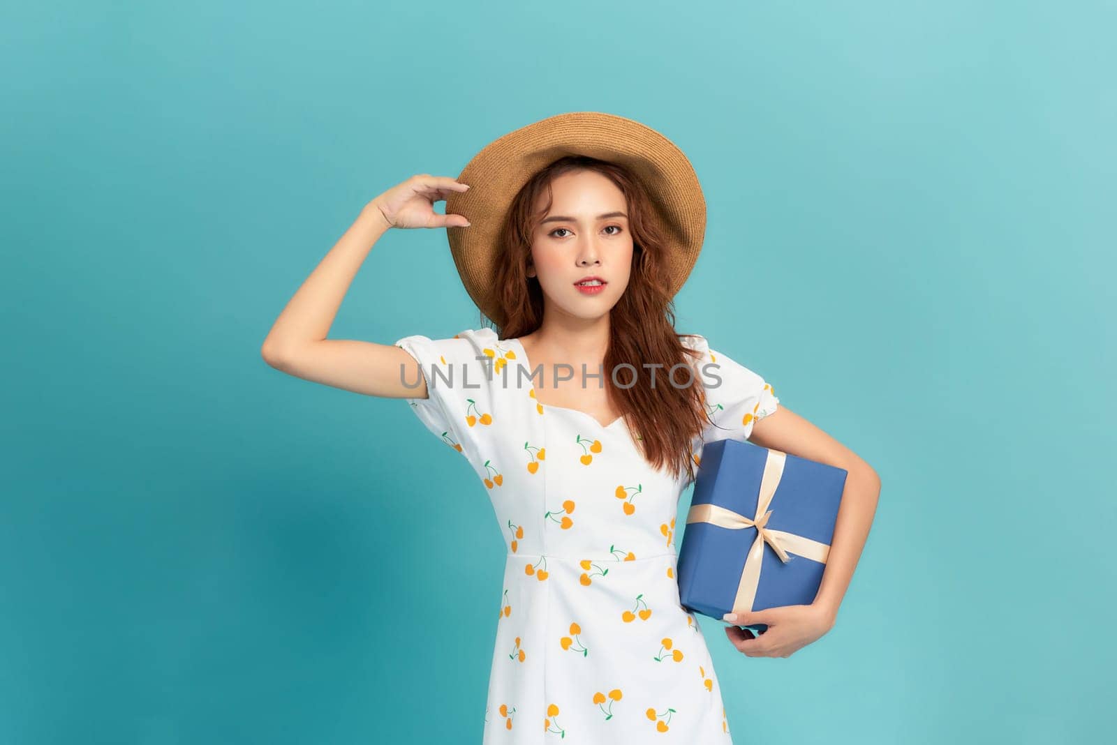 Portrait of a smiling young woman in summer dress holding gift box isolated over blue background by makidotvn