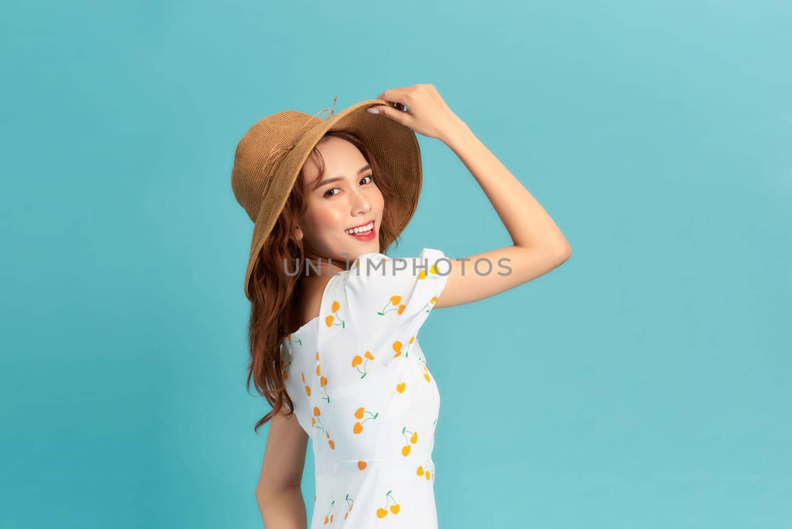 Cheerful young asian woman in summer dress and straw hat isolated on blue background. by makidotvn