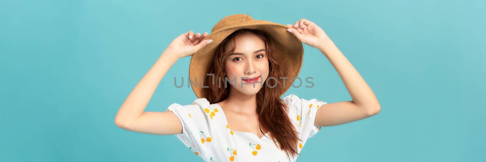 Cheerful young asian woman in summer dress and straw hat isolated on blue background.