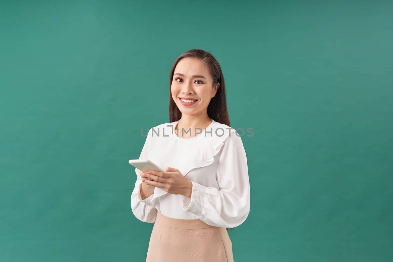 Portrait of a smiling casual woman holding smartphone over green background by makidotvn