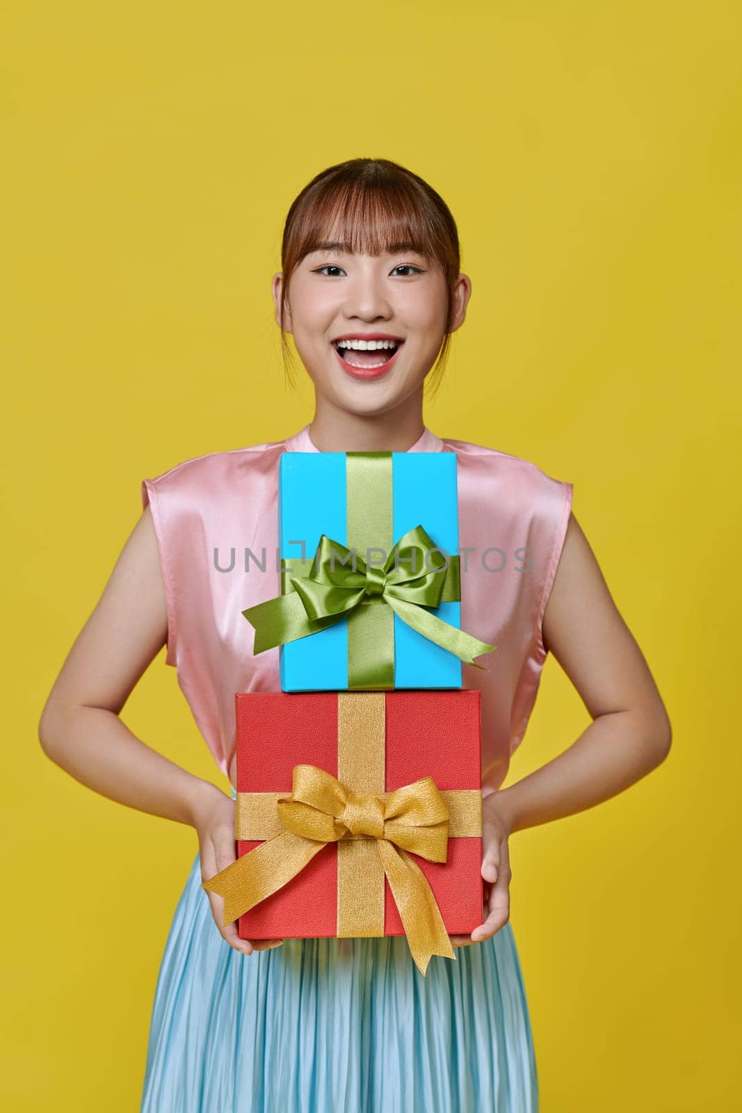 Smiling. Portrait of stylish woman emotionally posing with present boxes over yellow background