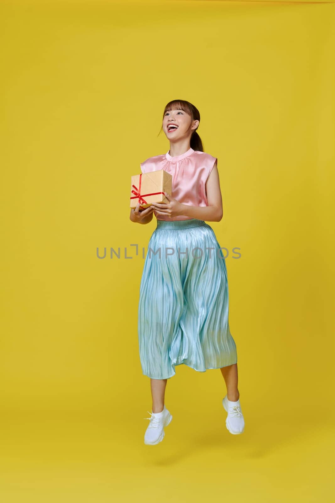 Full size profile photo of pretty  lady jump with present isolated on yellow background by makidotvn
