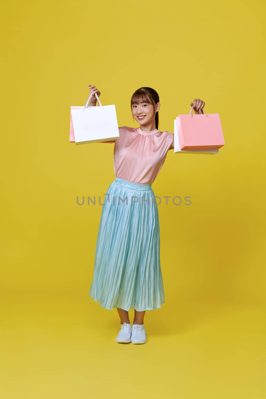 Pretty Asian woman carrying colorful shopping bags in purple color studio background