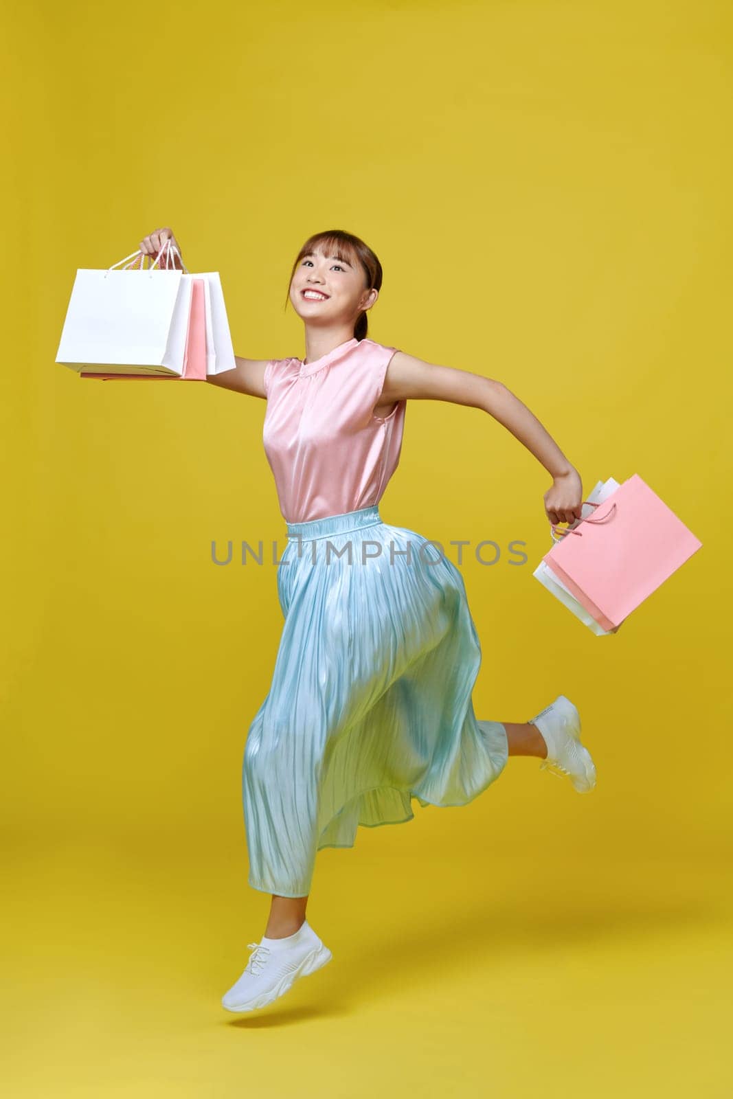beautiful girl in elegant spring dress holding shopping bags on yellow background by makidotvn