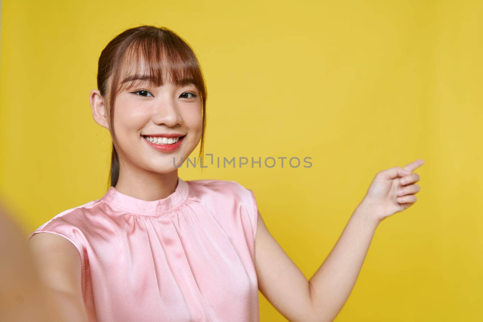 Dreamy cute young lady recording self video showing arm empty space isolated on yellow background by makidotvn