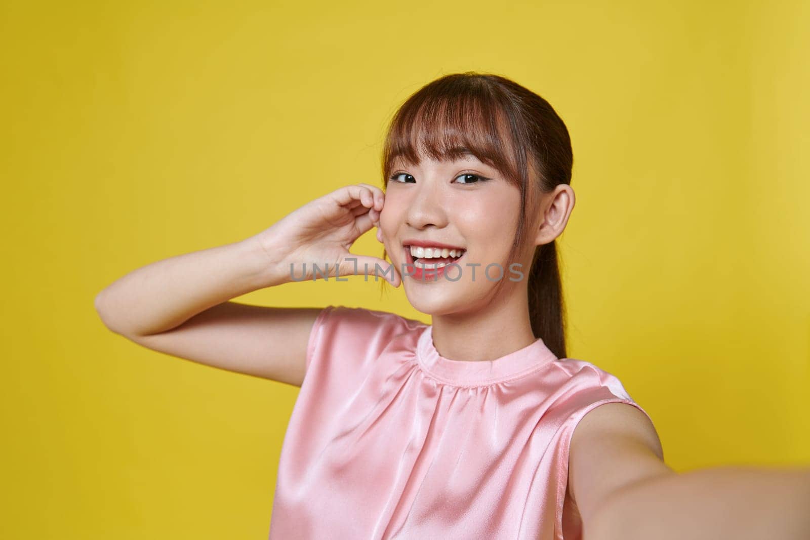 Young happy woman do selfie shot pov on mobile phone spread hands isolated on yellow by makidotvn
