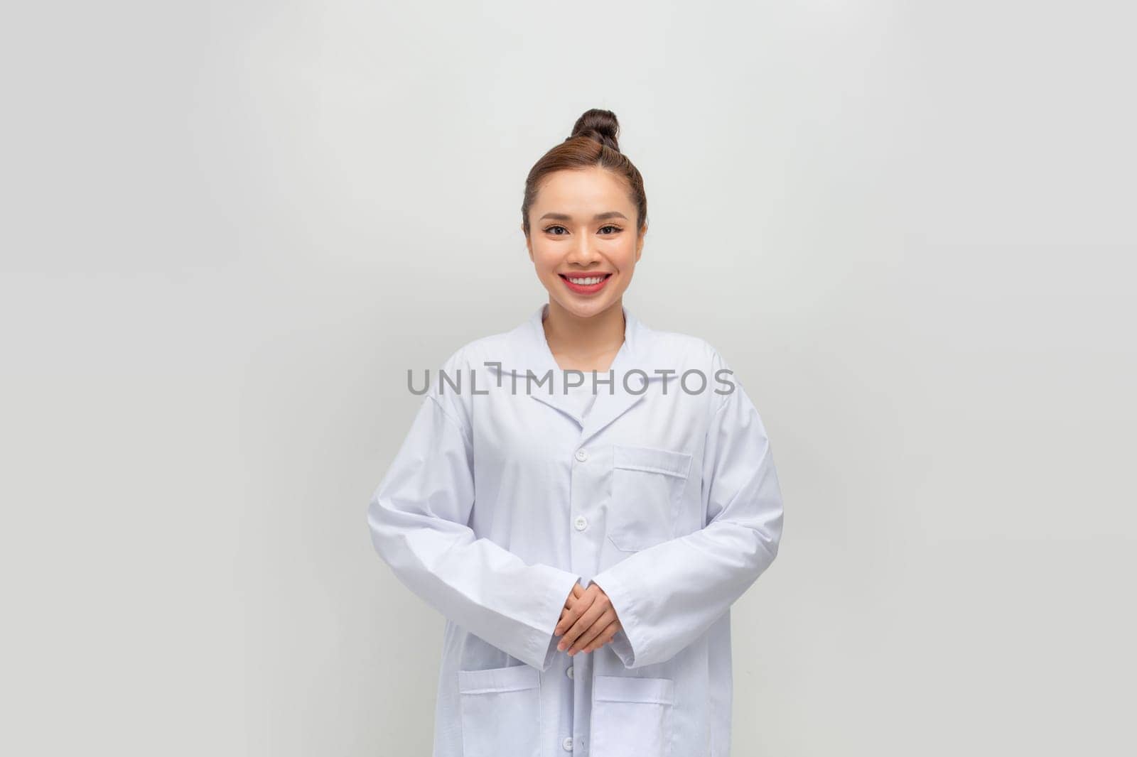 Happy young female doctor in medical uniform smiling while standing with folded arms