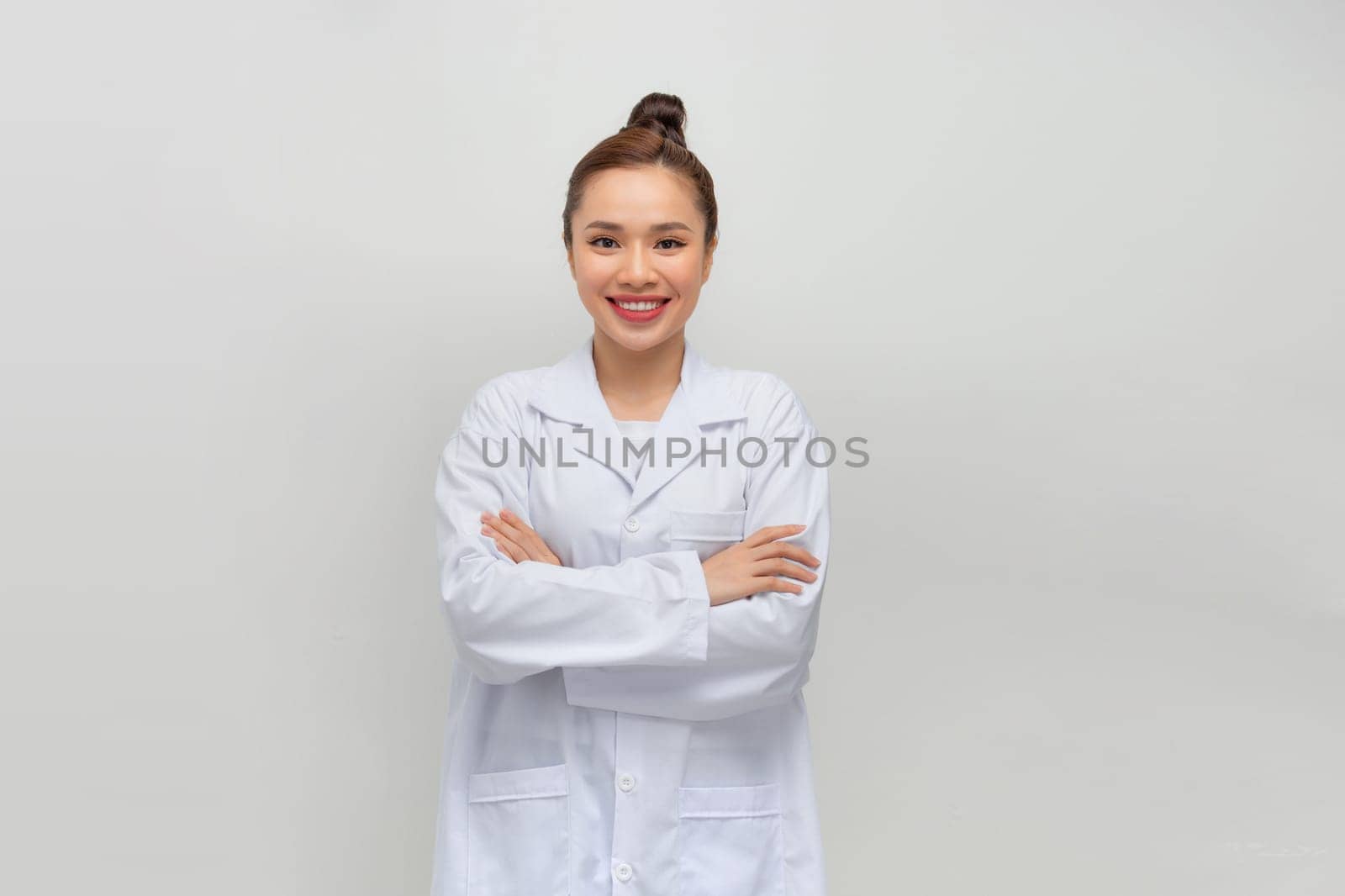 Happy young female doctor in medical uniform smiling while standing with folded arms by makidotvn