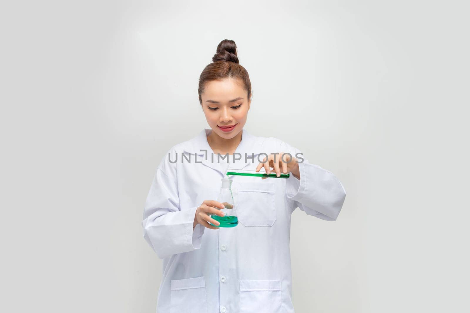 Female doctor in white uniform is holding flasks while standing against white background.