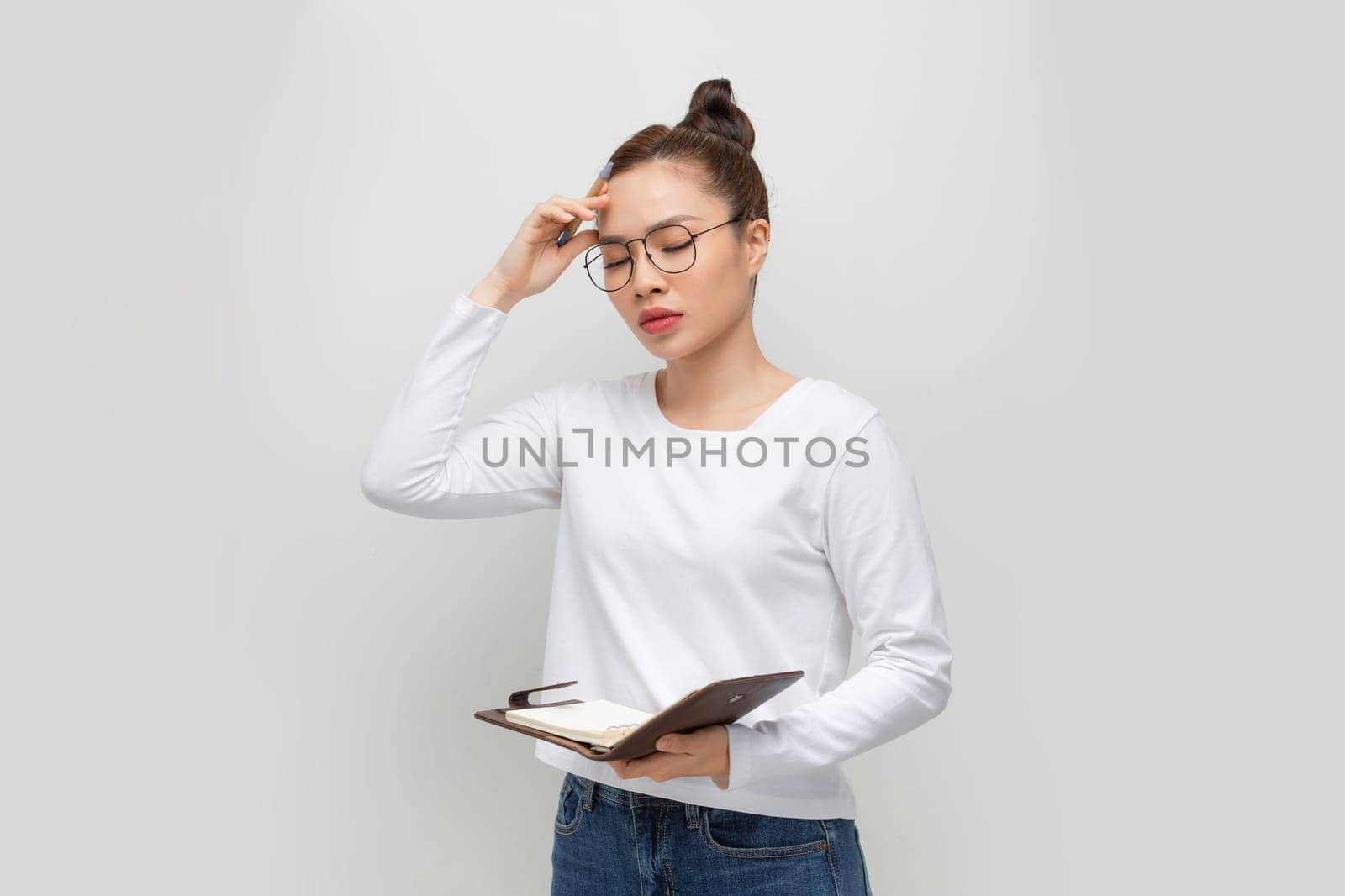 Intelligent asian lady in glasses taking notes, holding notepad and pen, standing over white