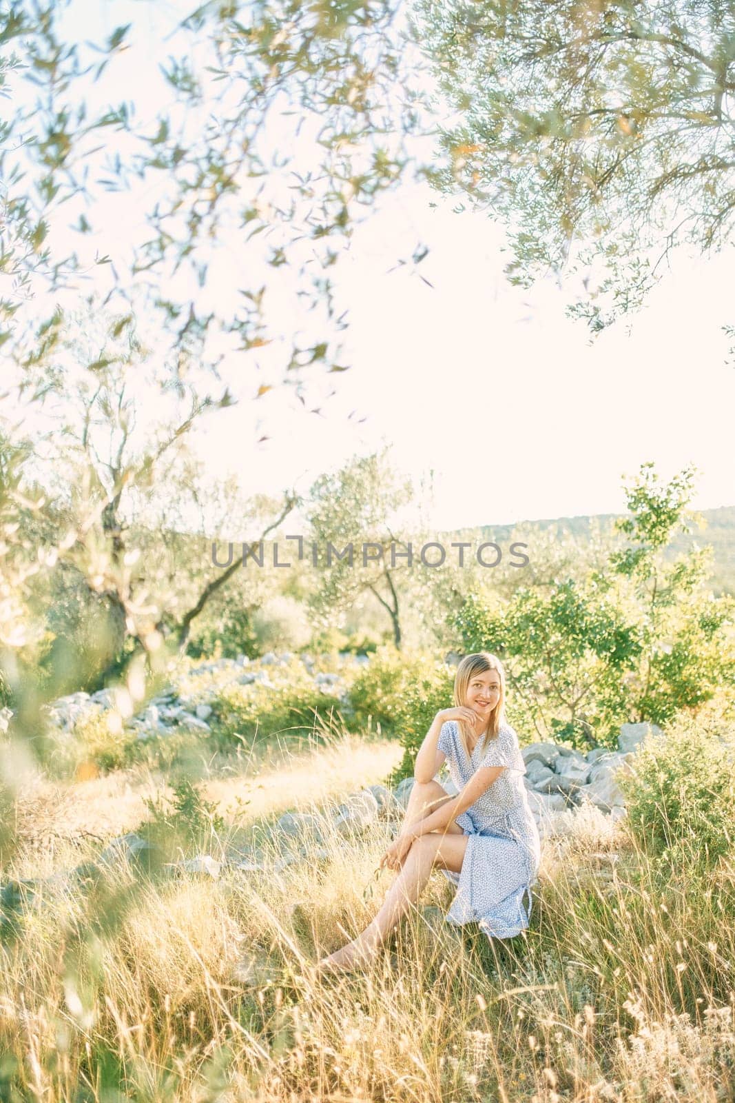 Smiling woman sitting on stones in the garden touching her chin with her fingers. High quality photo