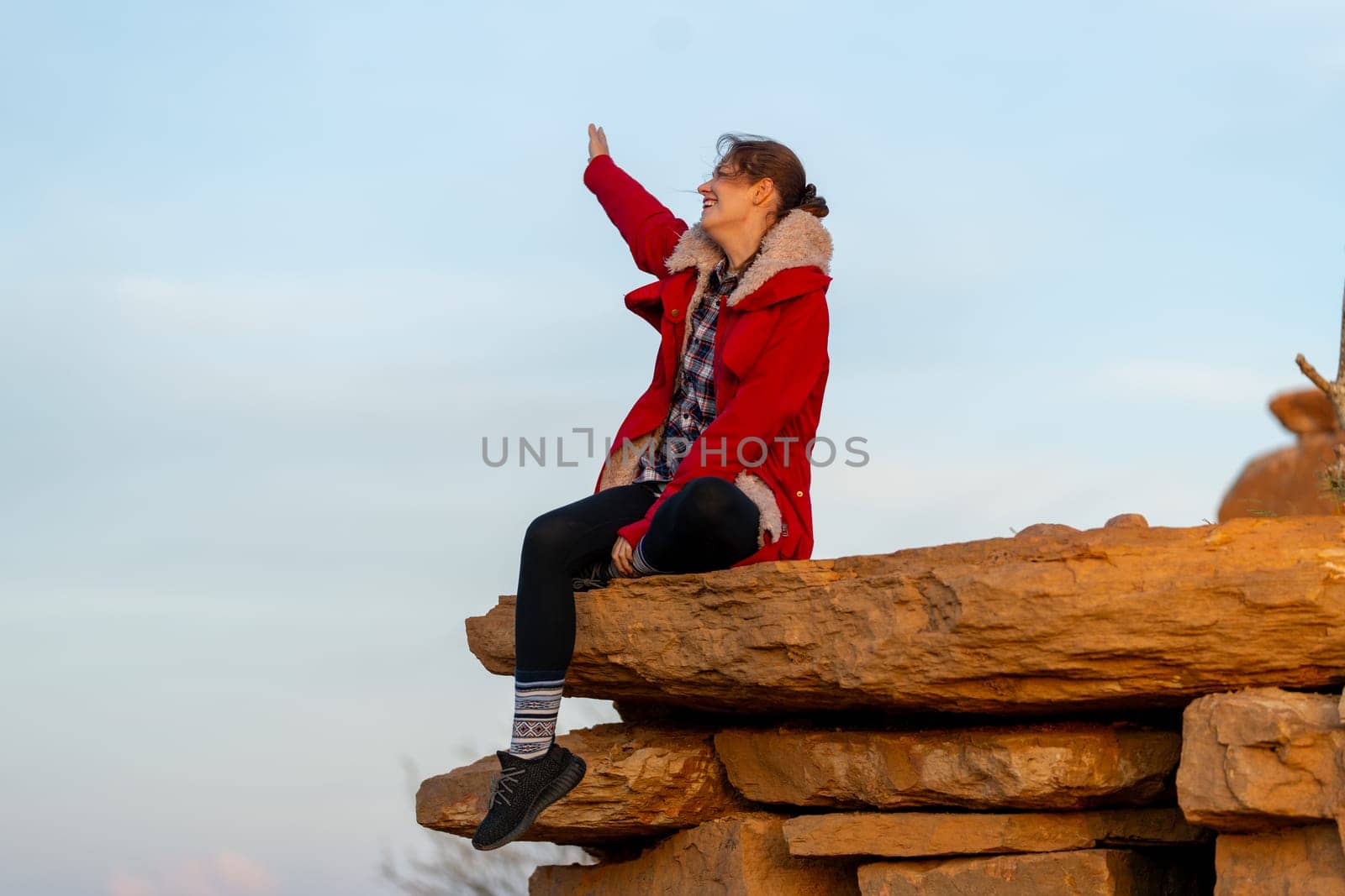 Beautiful woman sit on the rock near cliff on the mountain and raise her arm up with happiness and look forward with warm light in the morning.