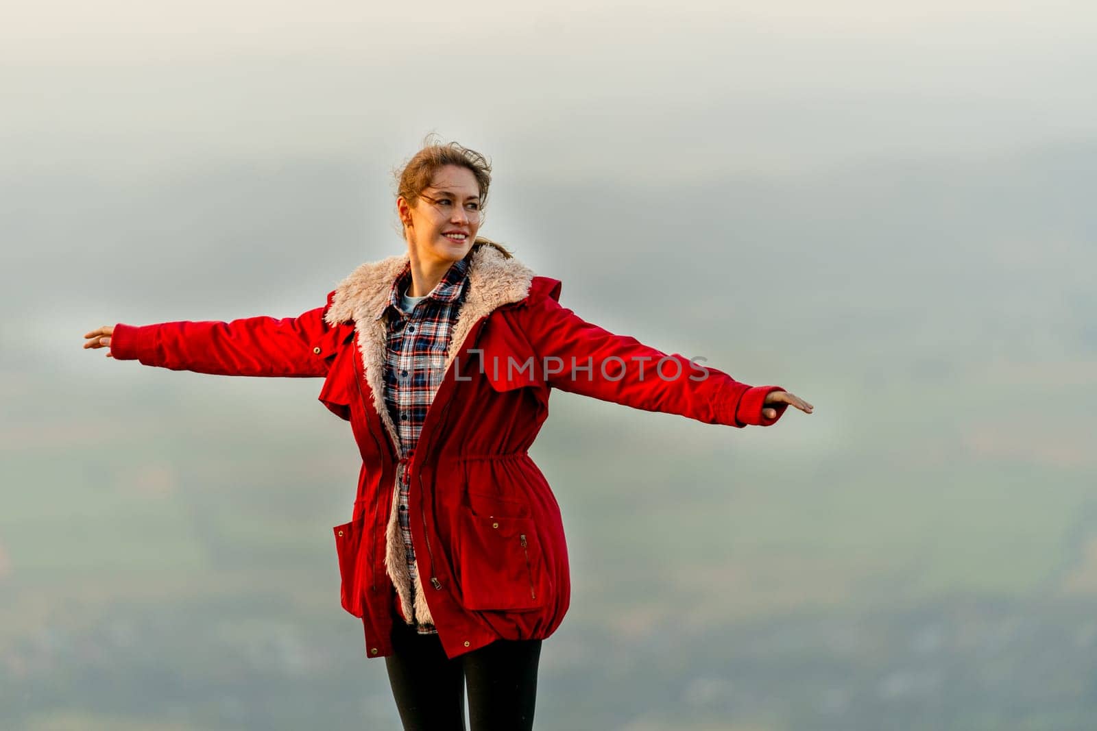 Close up beautiful woman stand near cliff with background of grass field and rural village area in view on the mountain with warm light of sun rise and she look to right side.