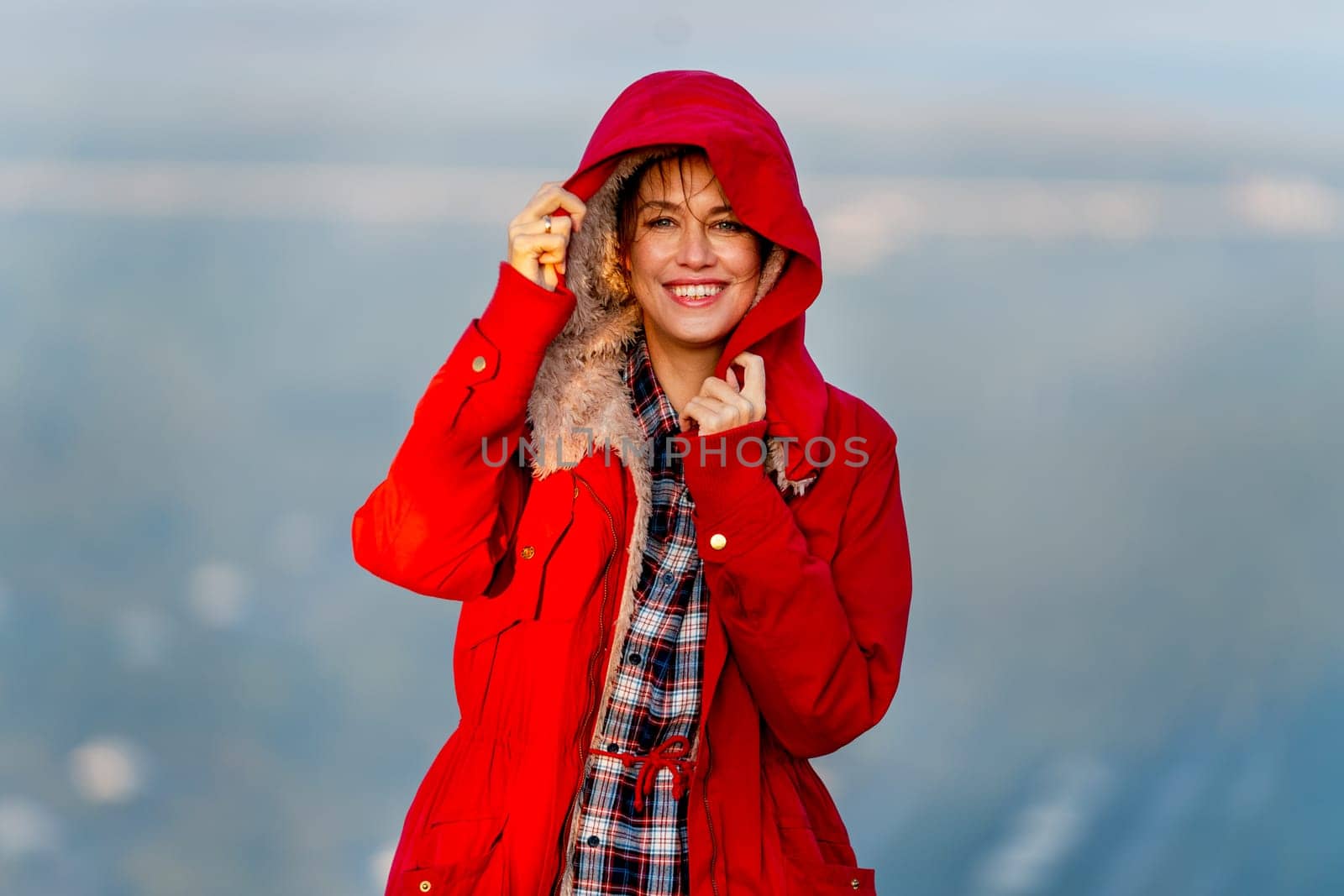 Close up beautiful Caucasian woman stand near cliff with hold coat hood and stay on the mountain with warm light of sun rise and she look happiness with smiling also look at camera.