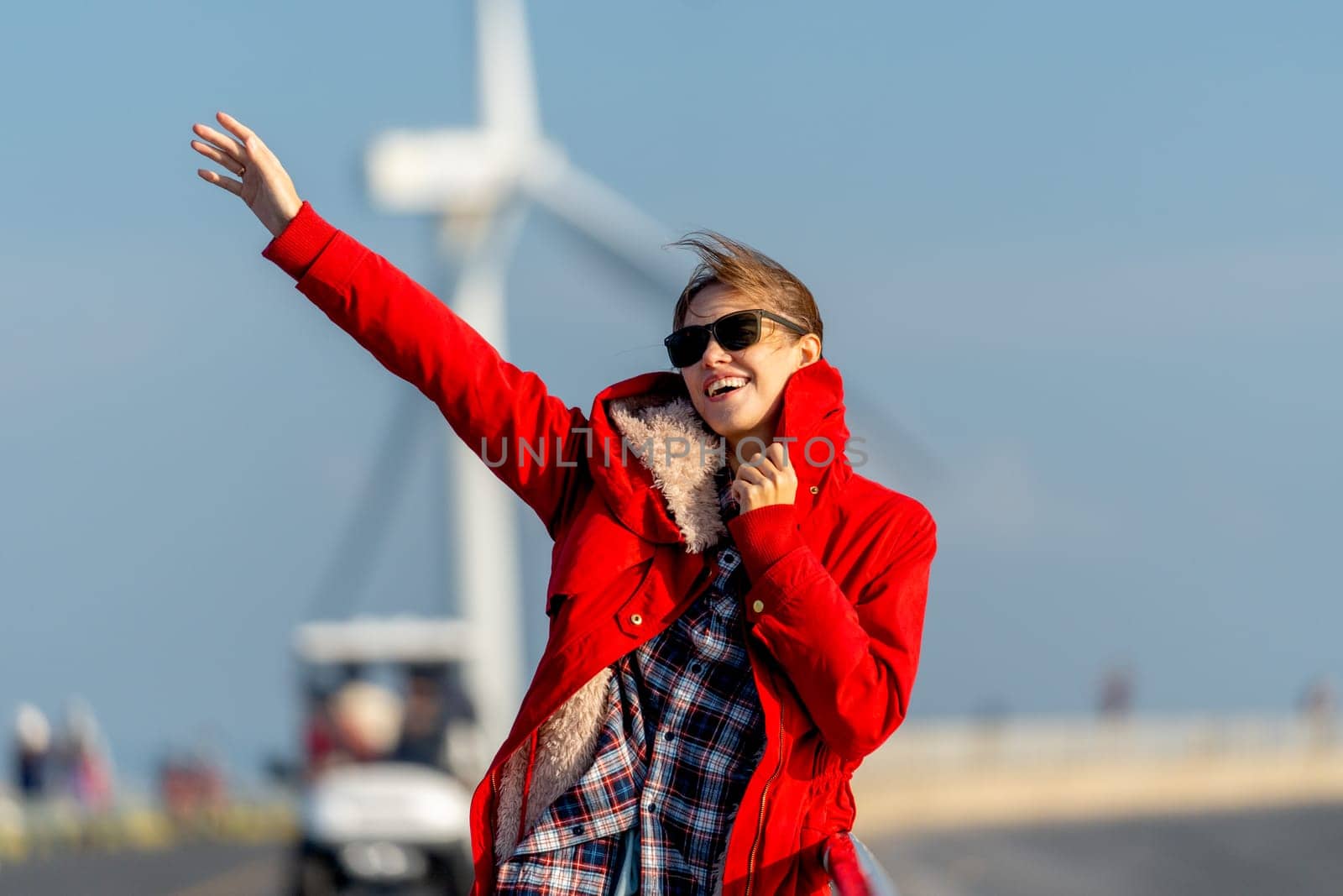Caucasian waman with sunglasses stand on the road in front of wind turbine or windmill also wave her hand with happiness.
