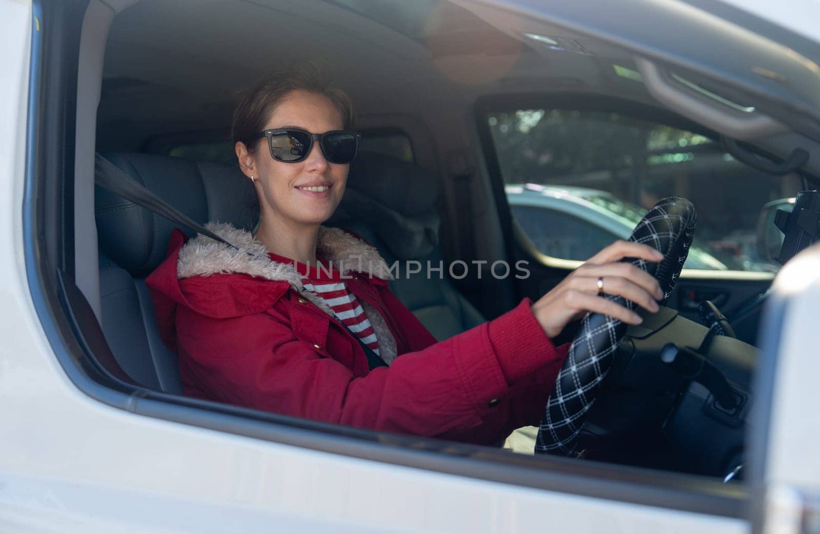 Beautiful woman with sunglasses sit in car and look at camera through window of car also look at camera with smiling in concept of safe drive on the road.