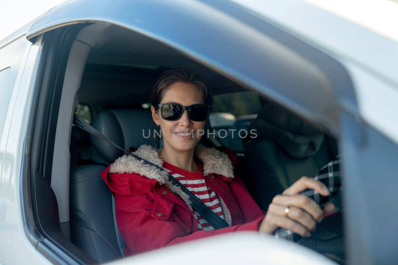 Beautiful woman with sunglasses sit in car and look at camera through window of car also look at camera with smiling in concept of safe drive on the road.