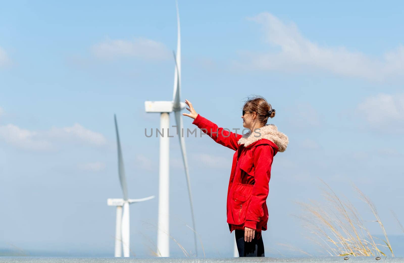Caucasian woman with sun glasses touch action with same position of wind turbine or windmill with blue sky in concept of green energy for good environment.