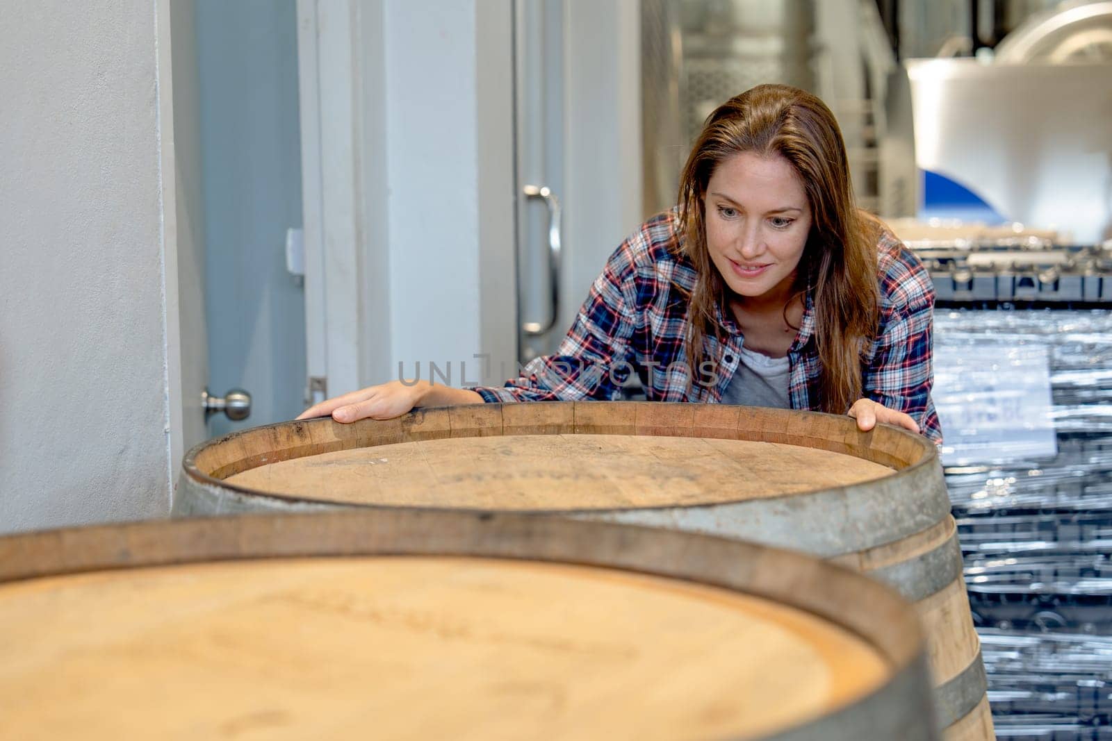 Winery worker woman stand near wine fermentation tank and check the product in modern factory.
